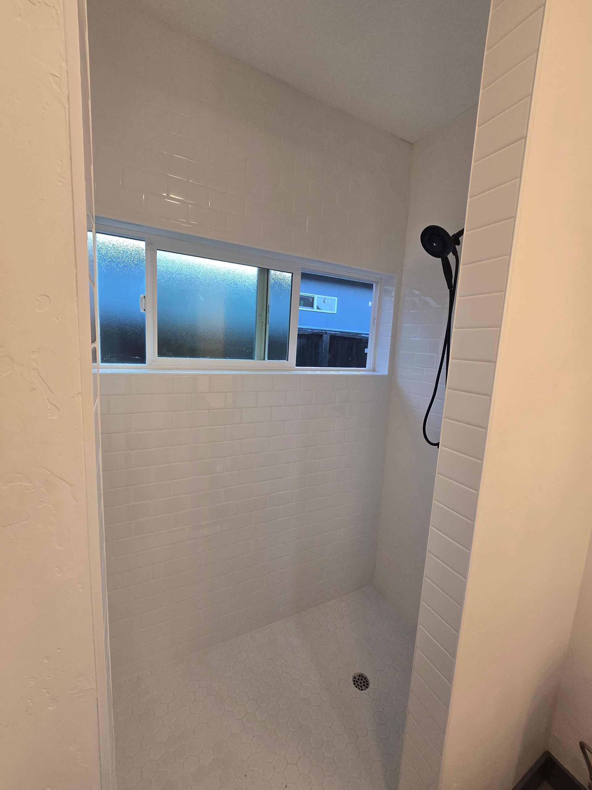 Small tiled shower with a frosted window and handheld showerhead on the right.