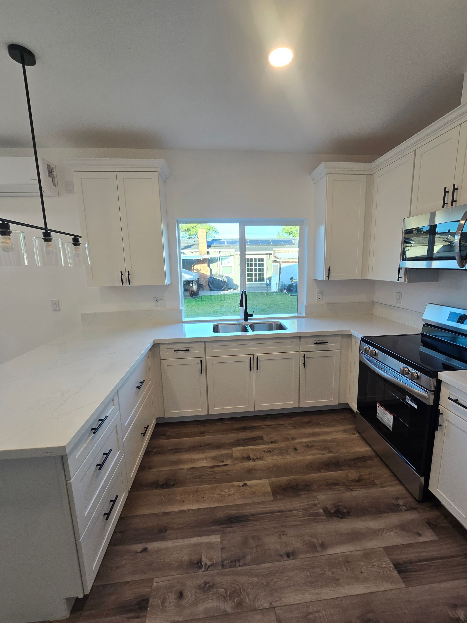 Bright white kitchen with dark wood floor, black stove, and window over the sink.