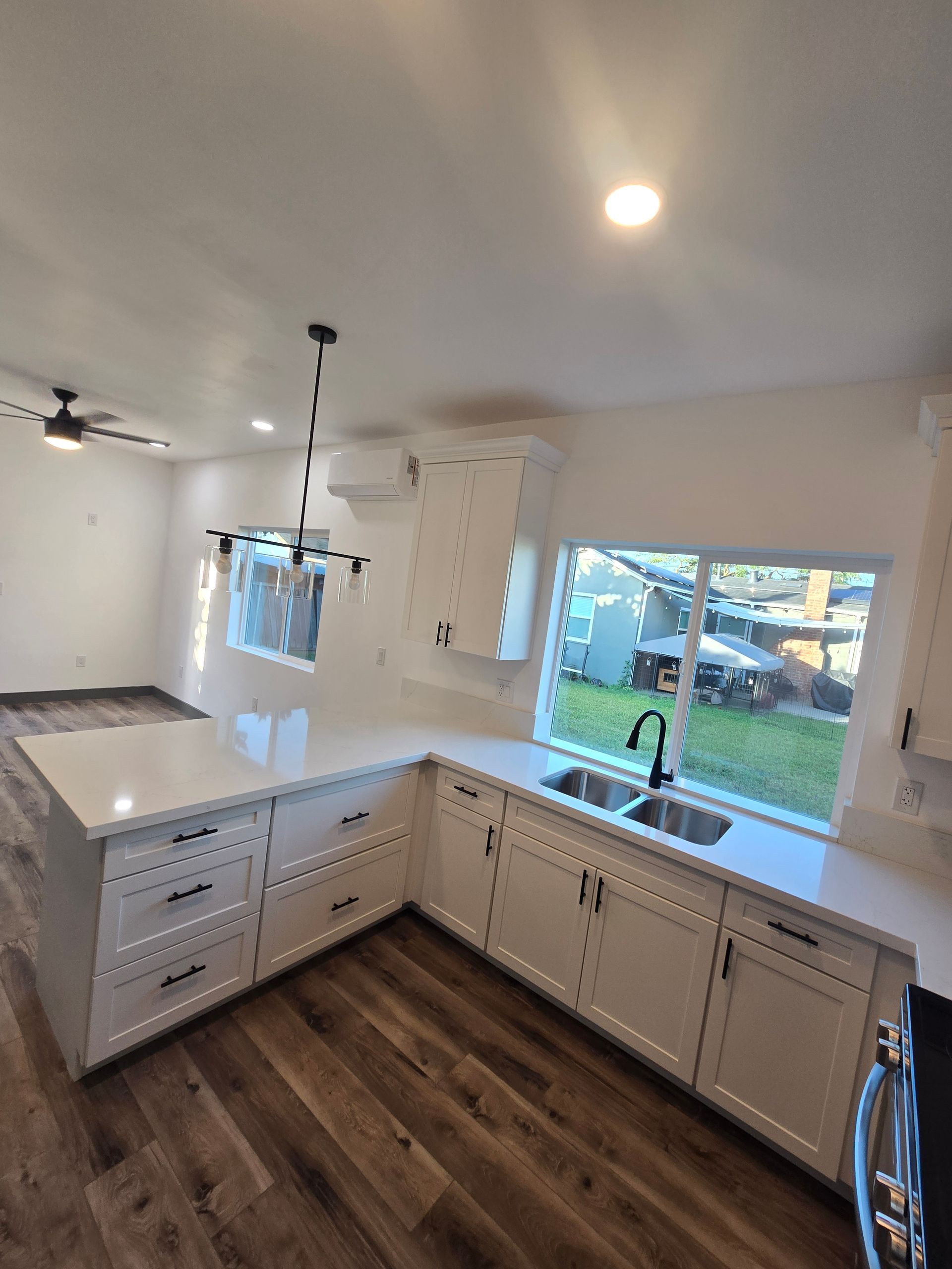 Bright kitchen with white cabinets, dark wood floor, island, sink, and large window overlooking a yard