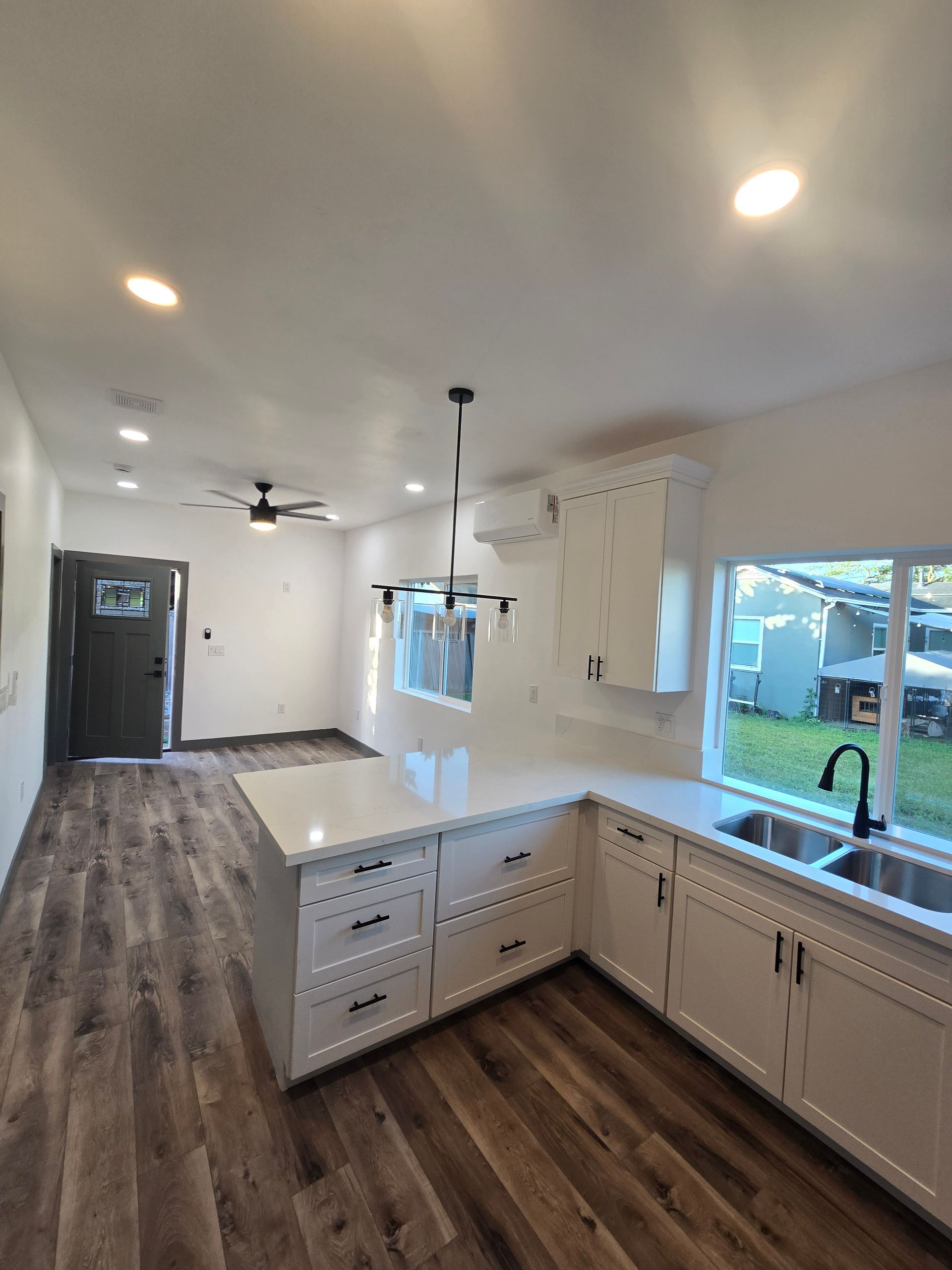 Bright modern kitchen with white cabinets, dark wood floors, island, sink, and large windows
