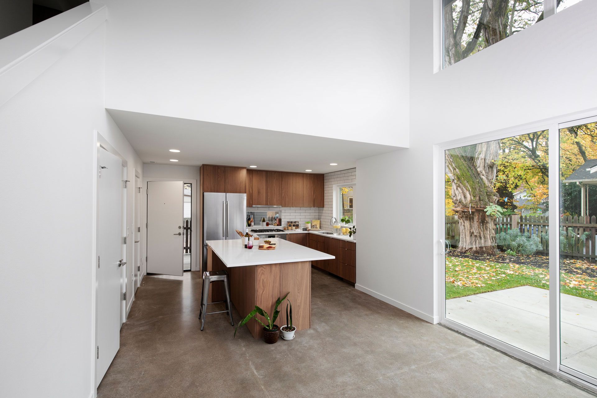 Modern open-plan kitchen and living area with wood island, white walls, and sliding glass doors to a garden.