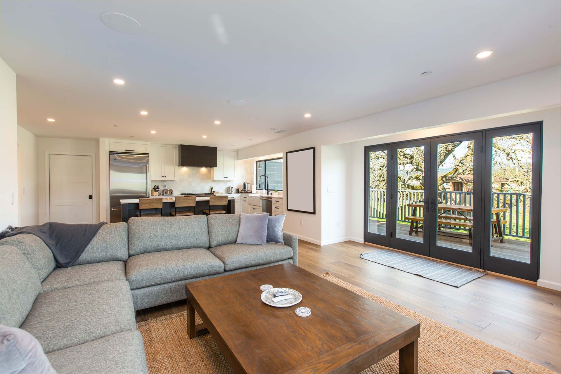 Bright living room with gray sectional, wood coffee table, open kitchen, and glass doors to a patio.