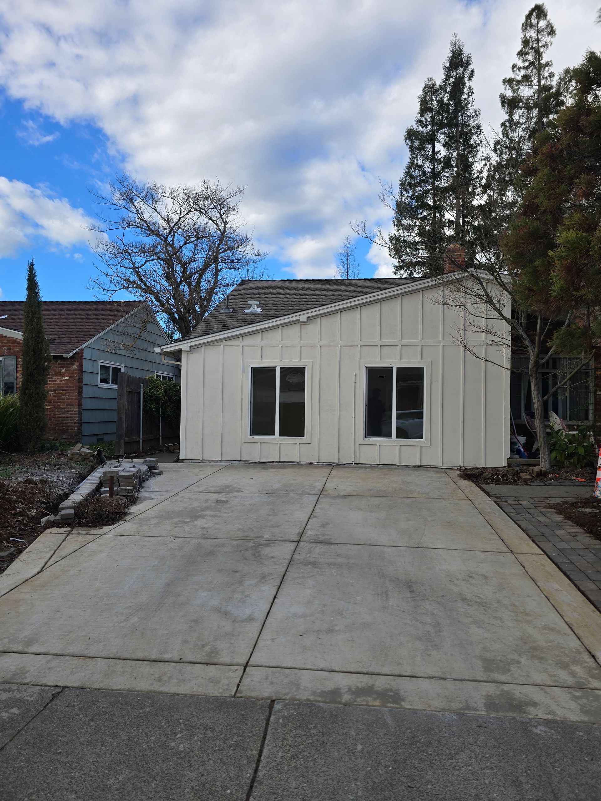 Small beige house with a driveway, surrounded by trees under a cloudy sky