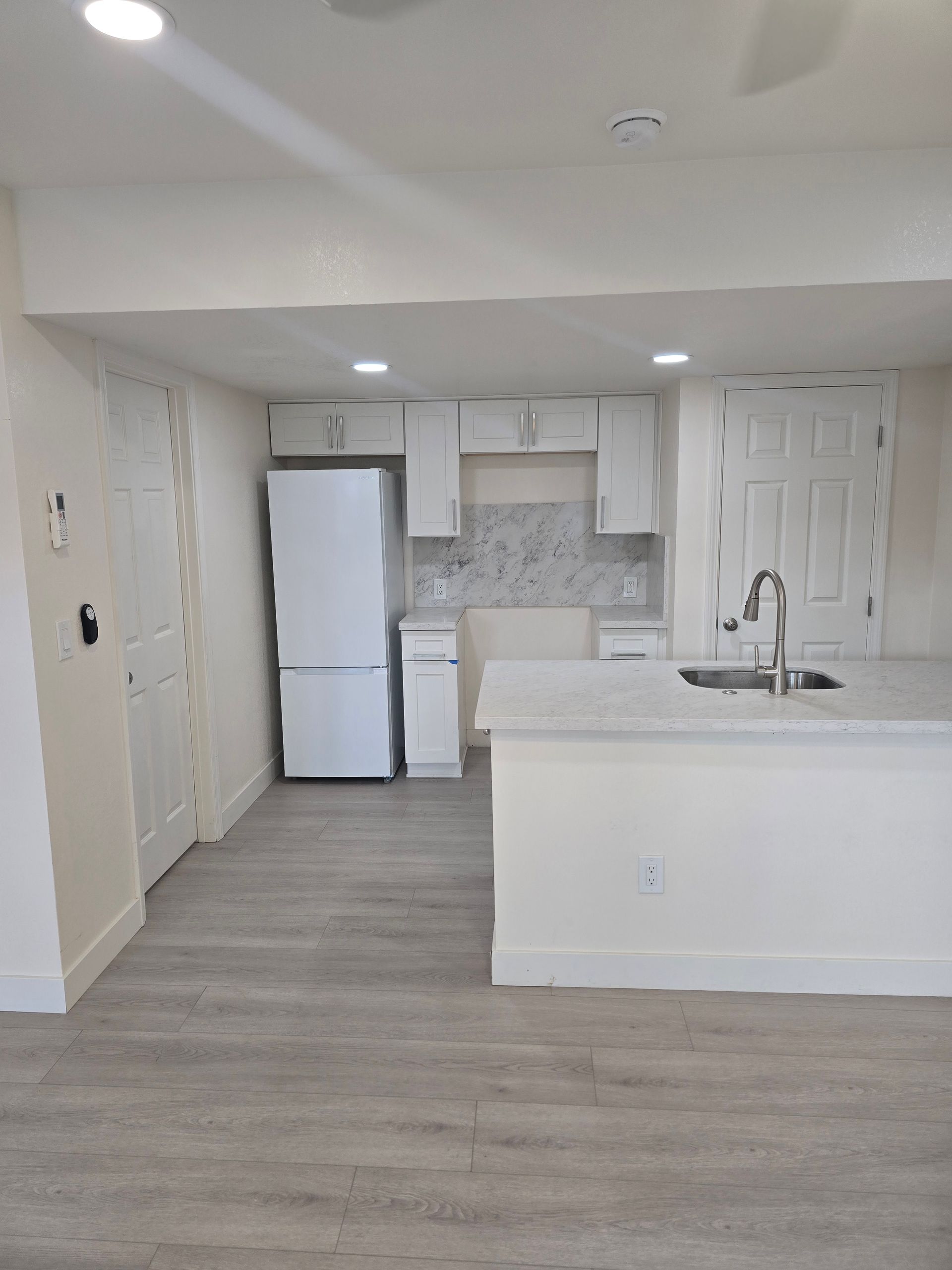 Modern kitchen with white cabinets, gray flooring, island sink, and stainless steel fridge