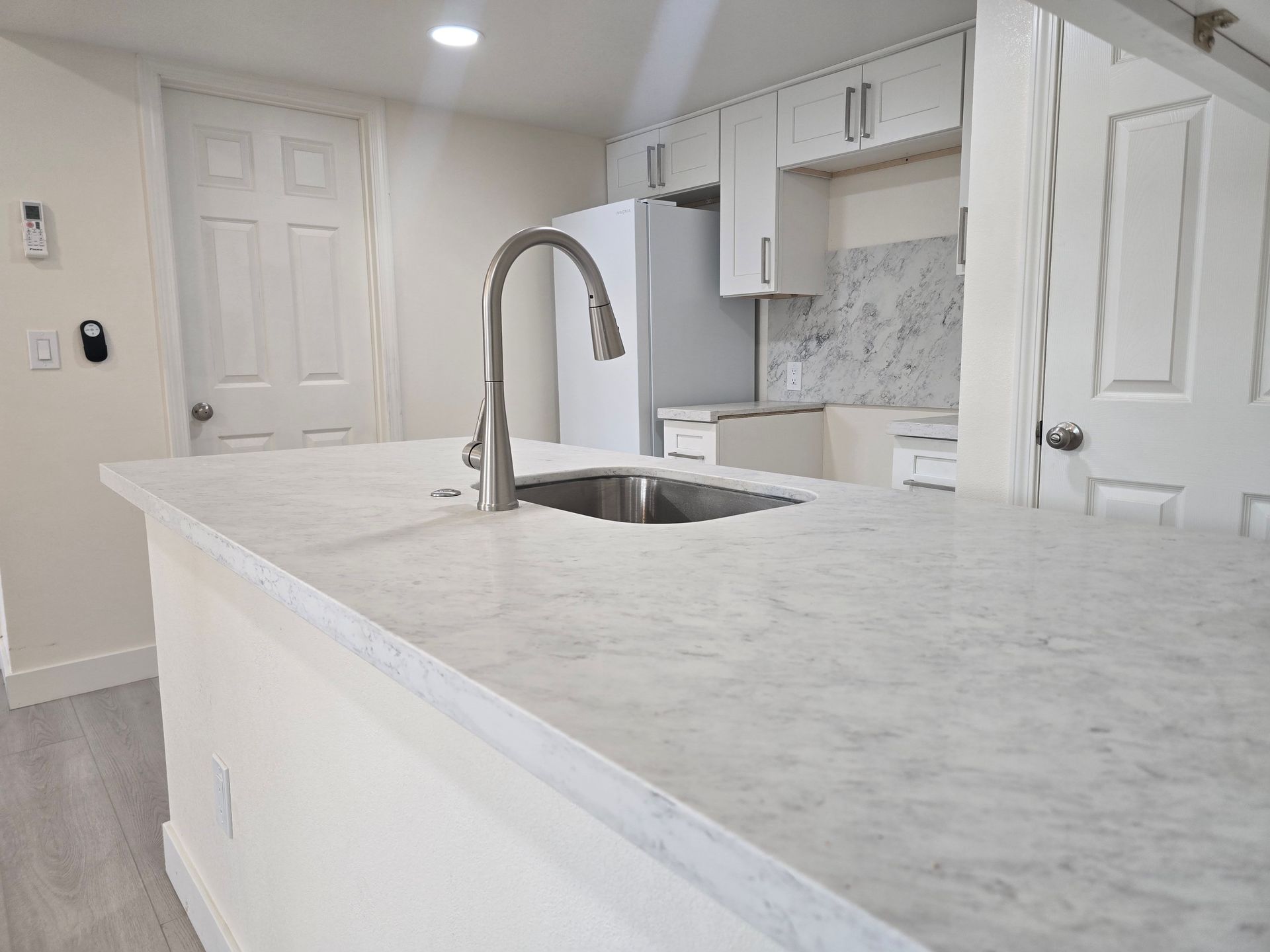 Bright modern kitchen with white cabinets, marble island, and stainless steel faucet