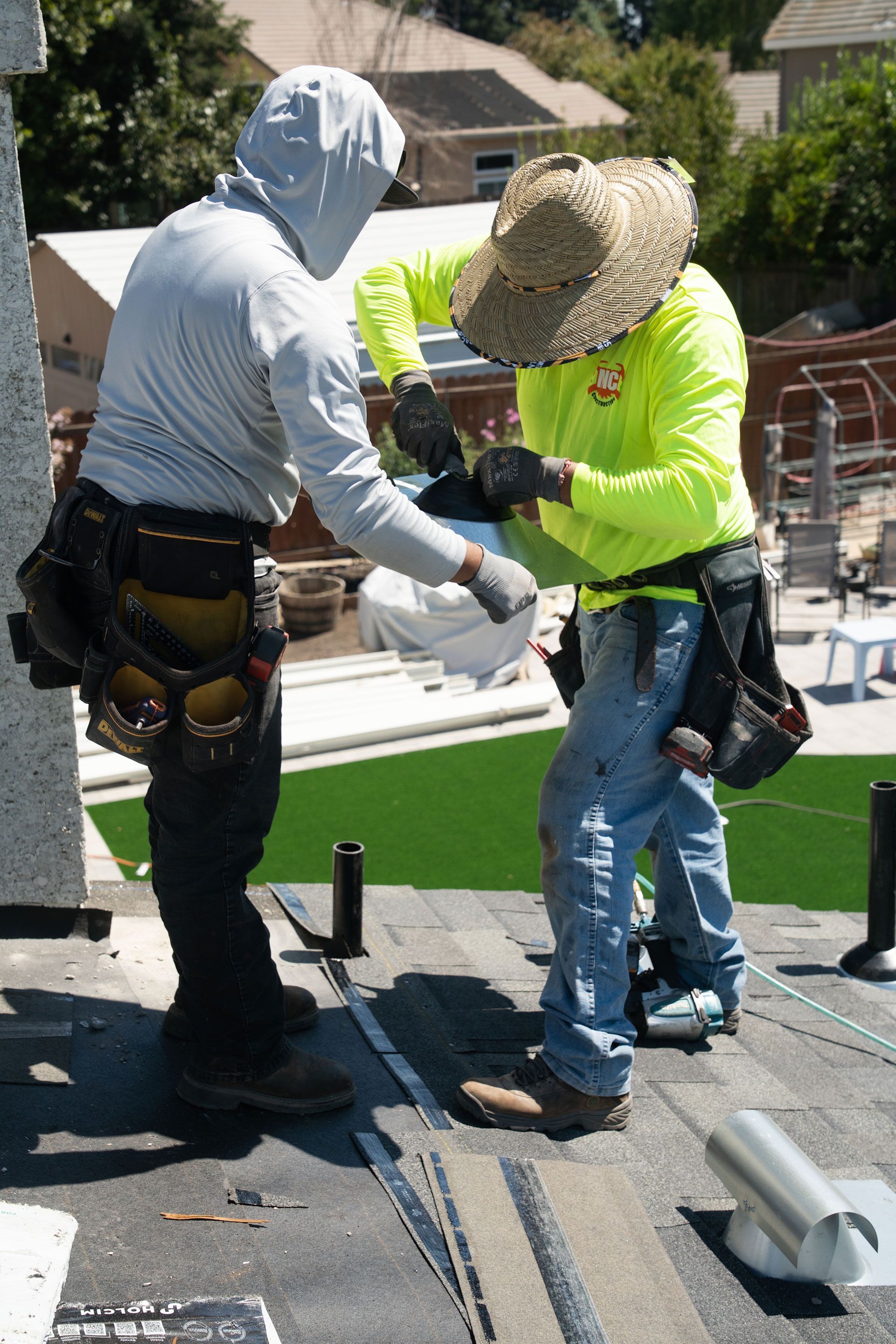 Two workers on a rooftop, one in a neon shirt and straw hat, handling materials near solar panels.
