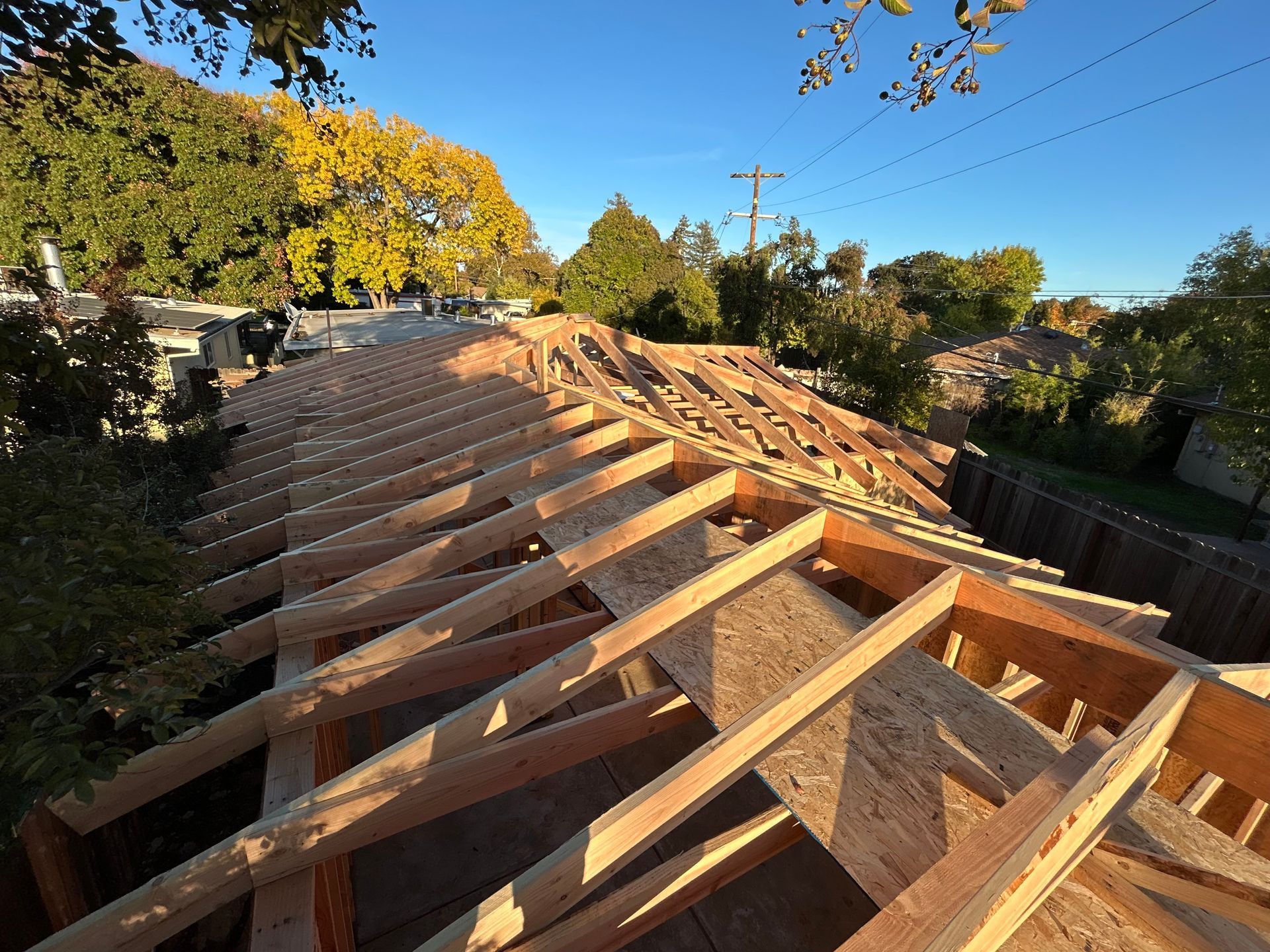 Roof framing under construction on a house, with exposed wooden beams against a clear blue sky.
