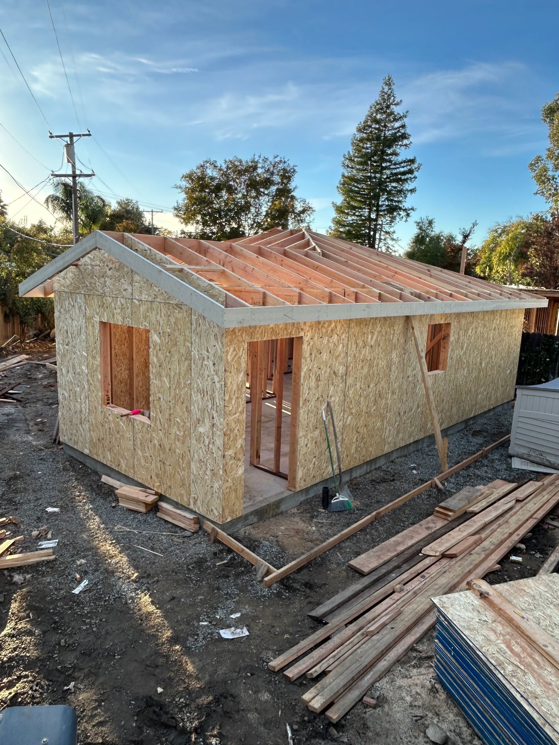 Partially built small house with plywood walls, rust-colored roof, and construction materials around it
