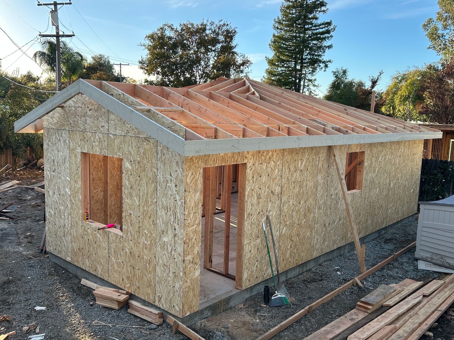 Small unfinished wooden house with OSB siding and roof sheathing under construction outdoors.