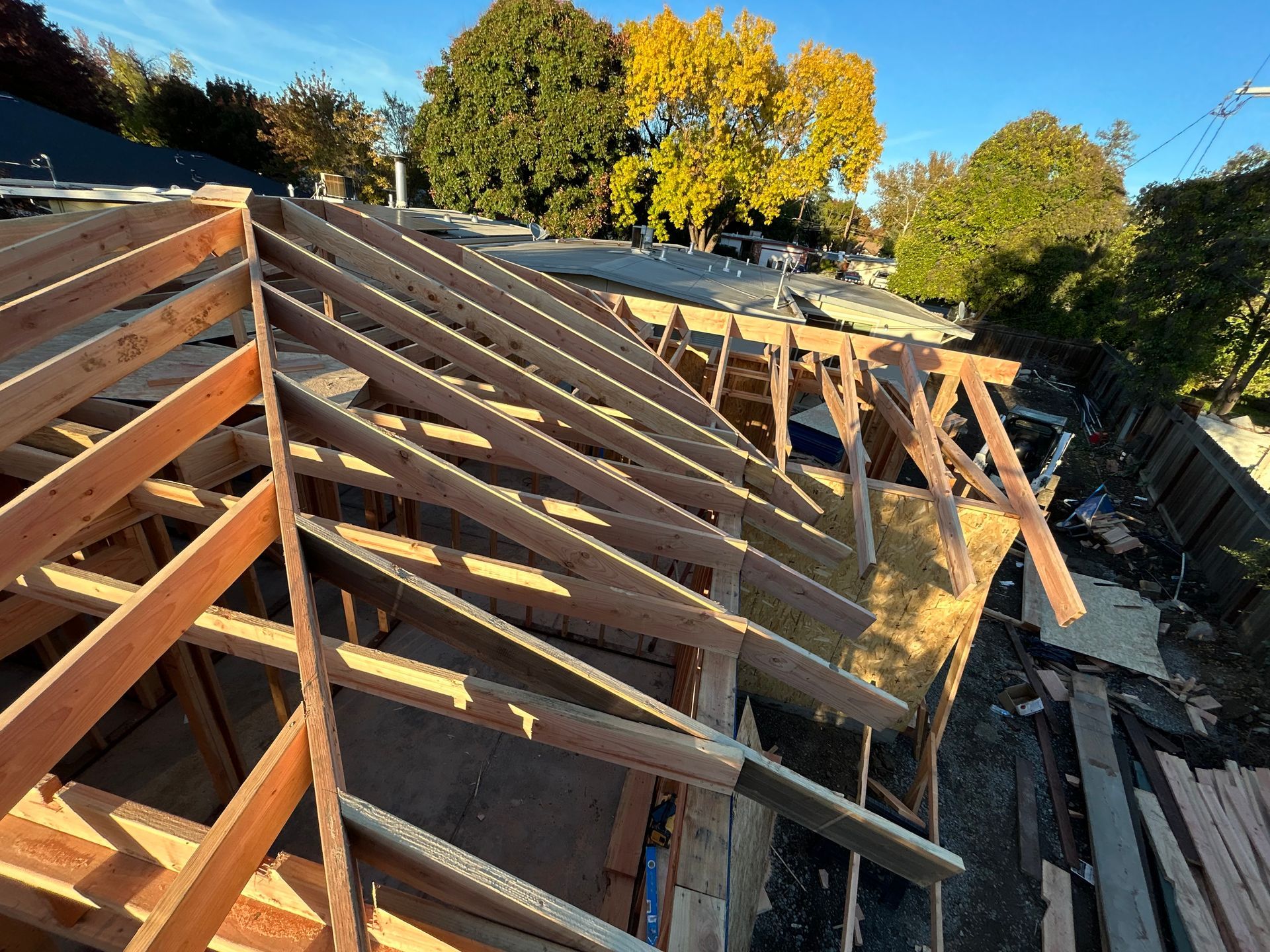 Roof framing under construction with exposed wooden trusses and autumn trees in the background