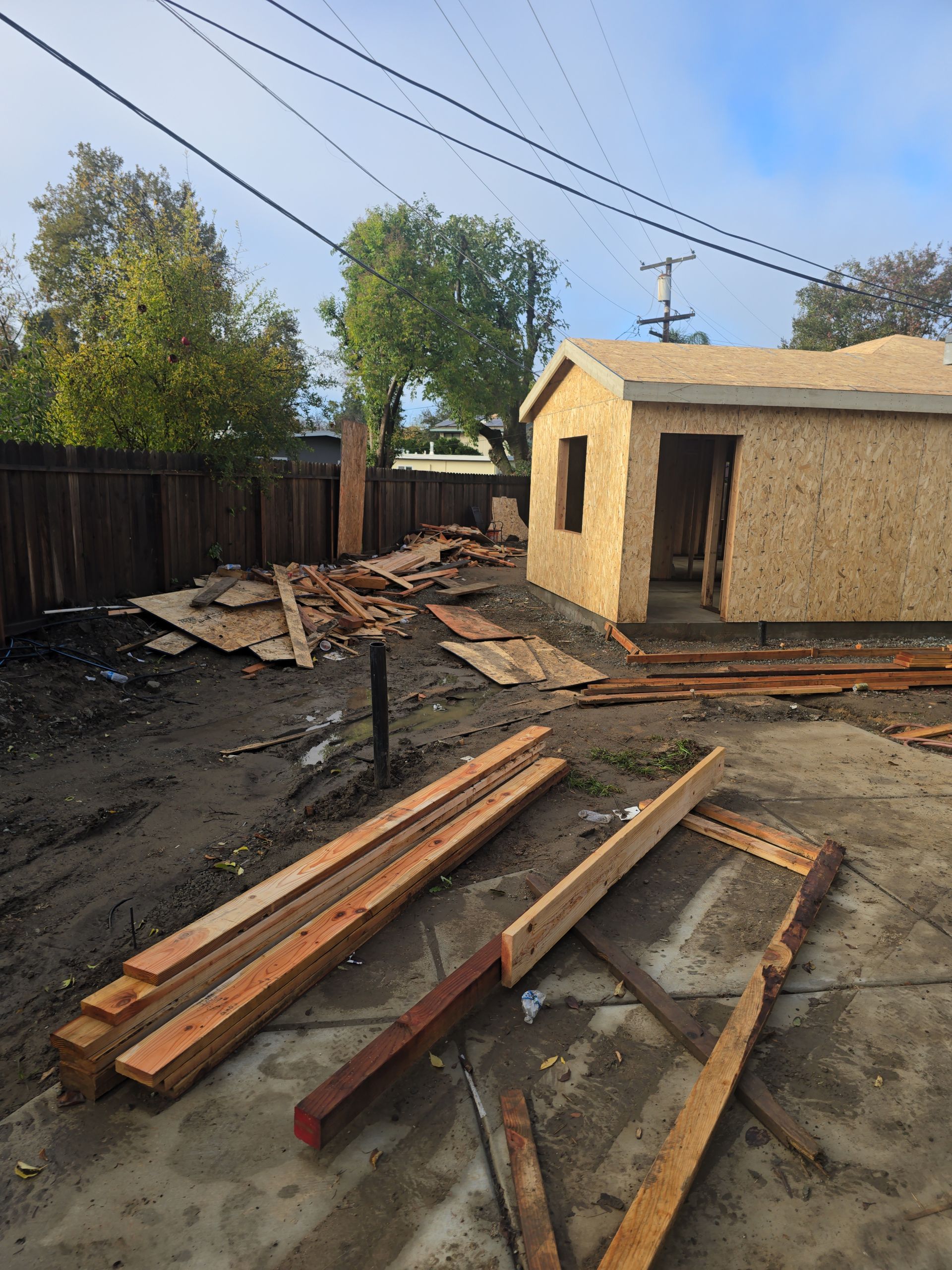 Backyard with scattered lumber and debris beside a small shed and wooden fence after storm damage