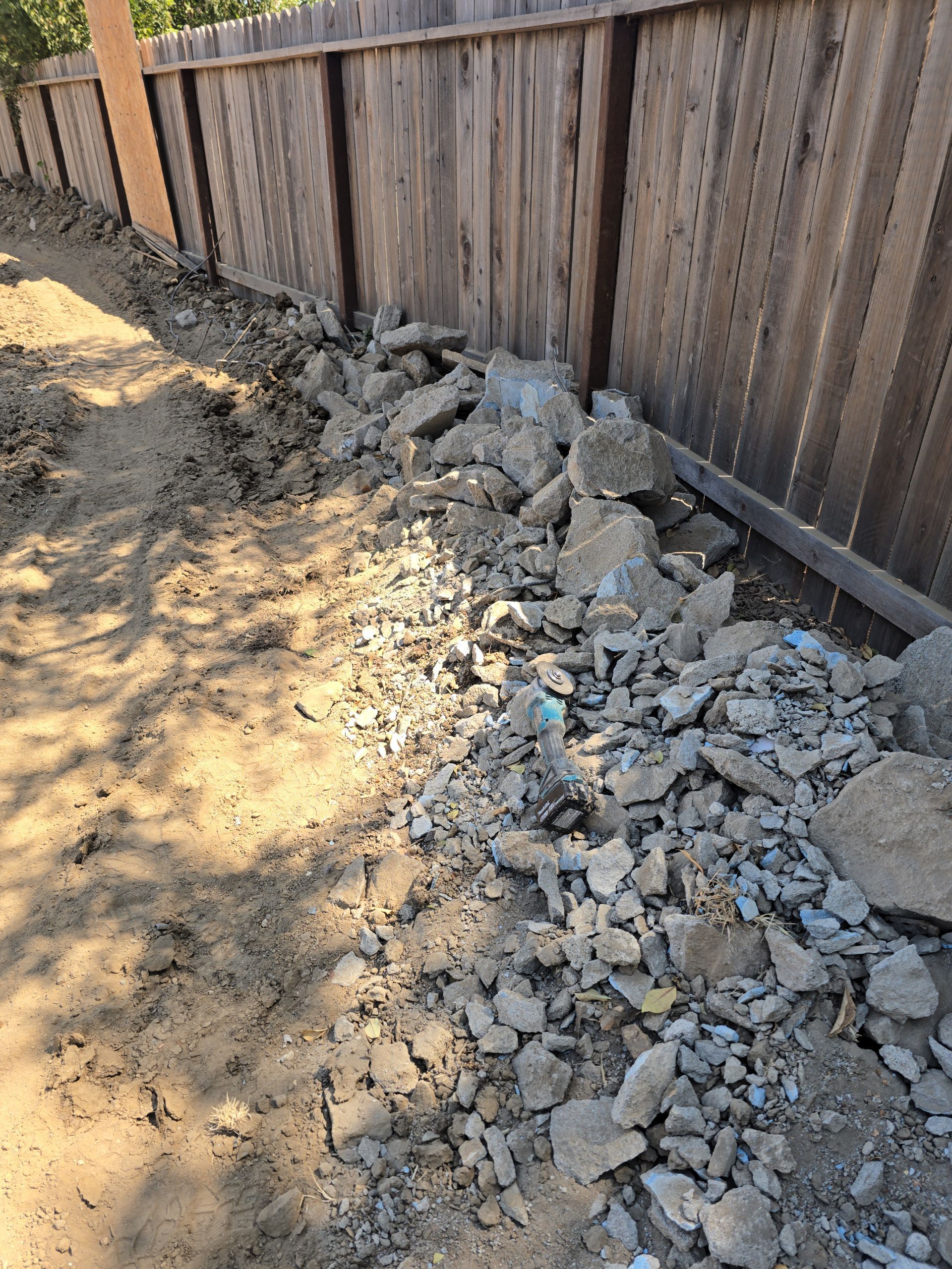 Rubble and broken concrete piled along a wooden fence beside a dirt path.