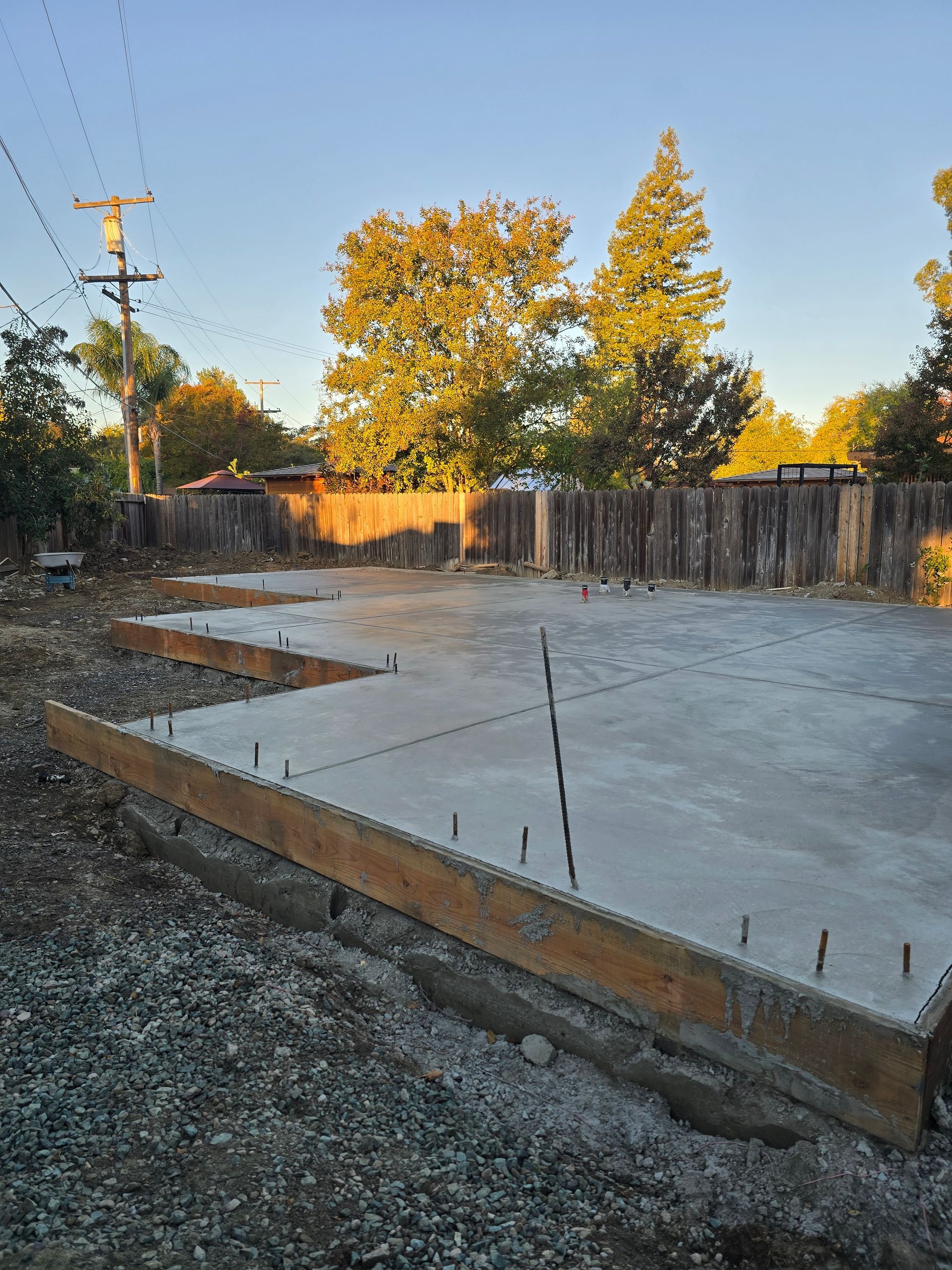 Fresh concrete slab foundation with rebar, beside a wooden fence at sunset
