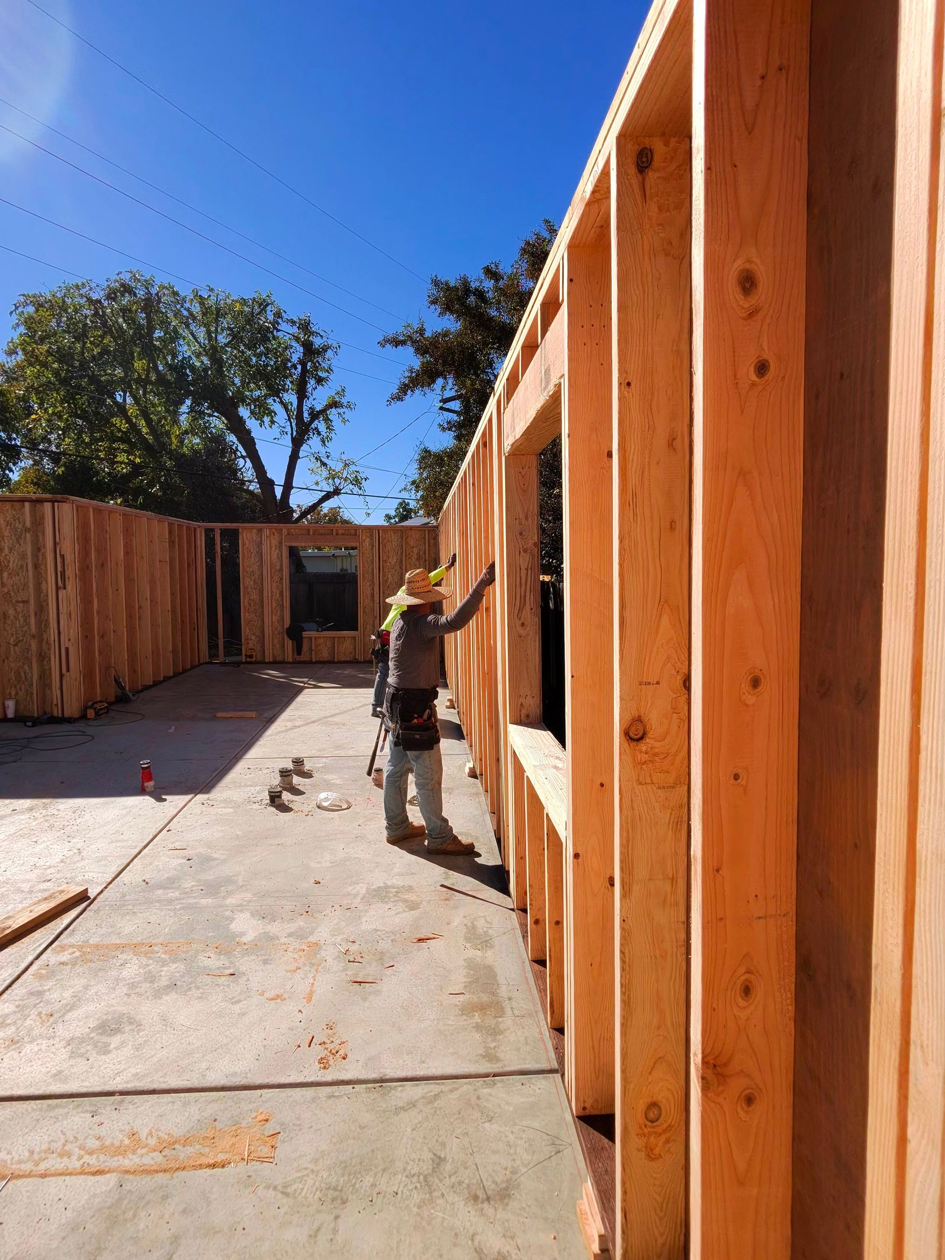 Wood-framed building under construction with a worker in a sunlit concrete walkway
