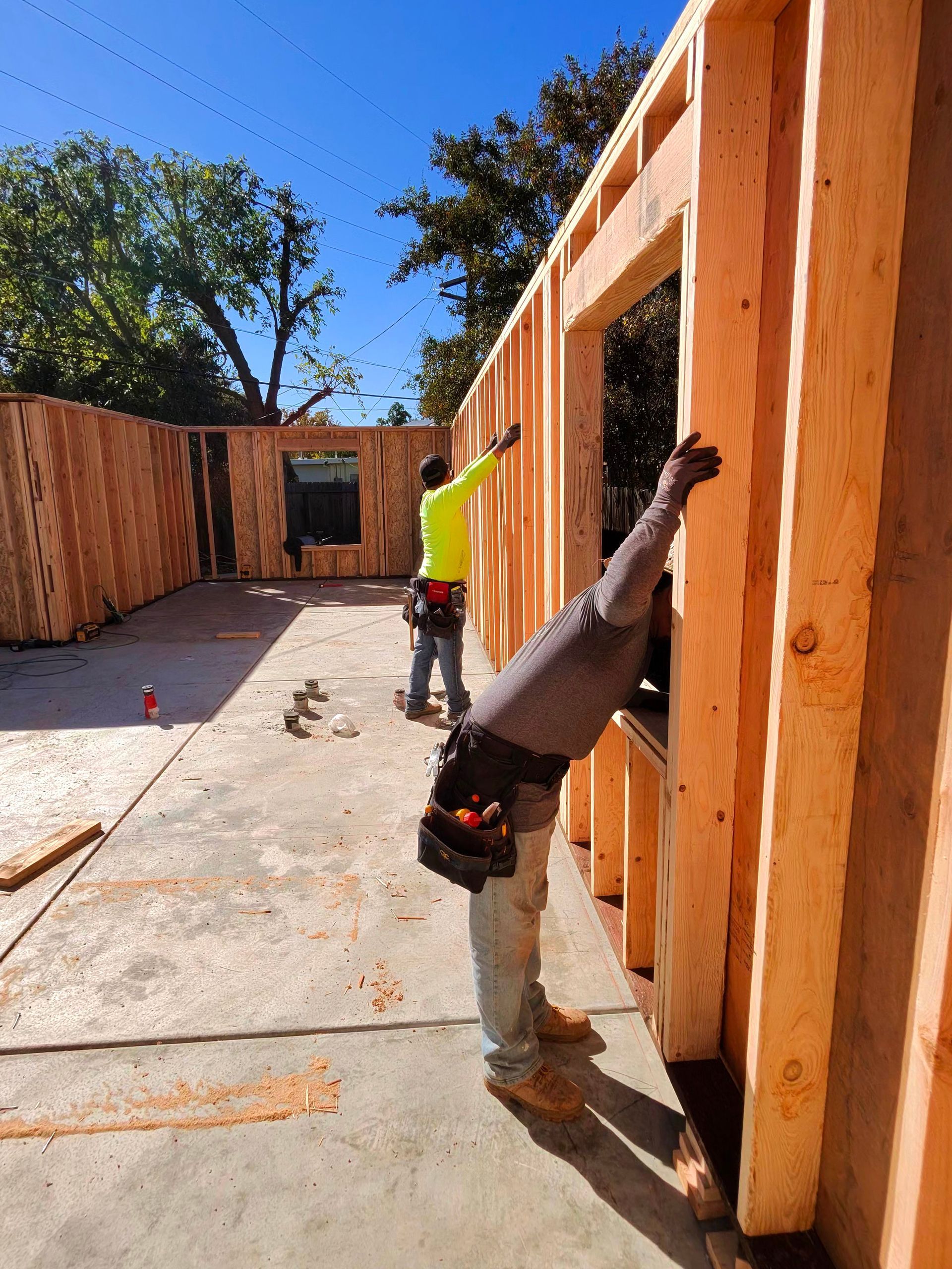 Workers framing wooden walls at a construction site under a clear blue sky