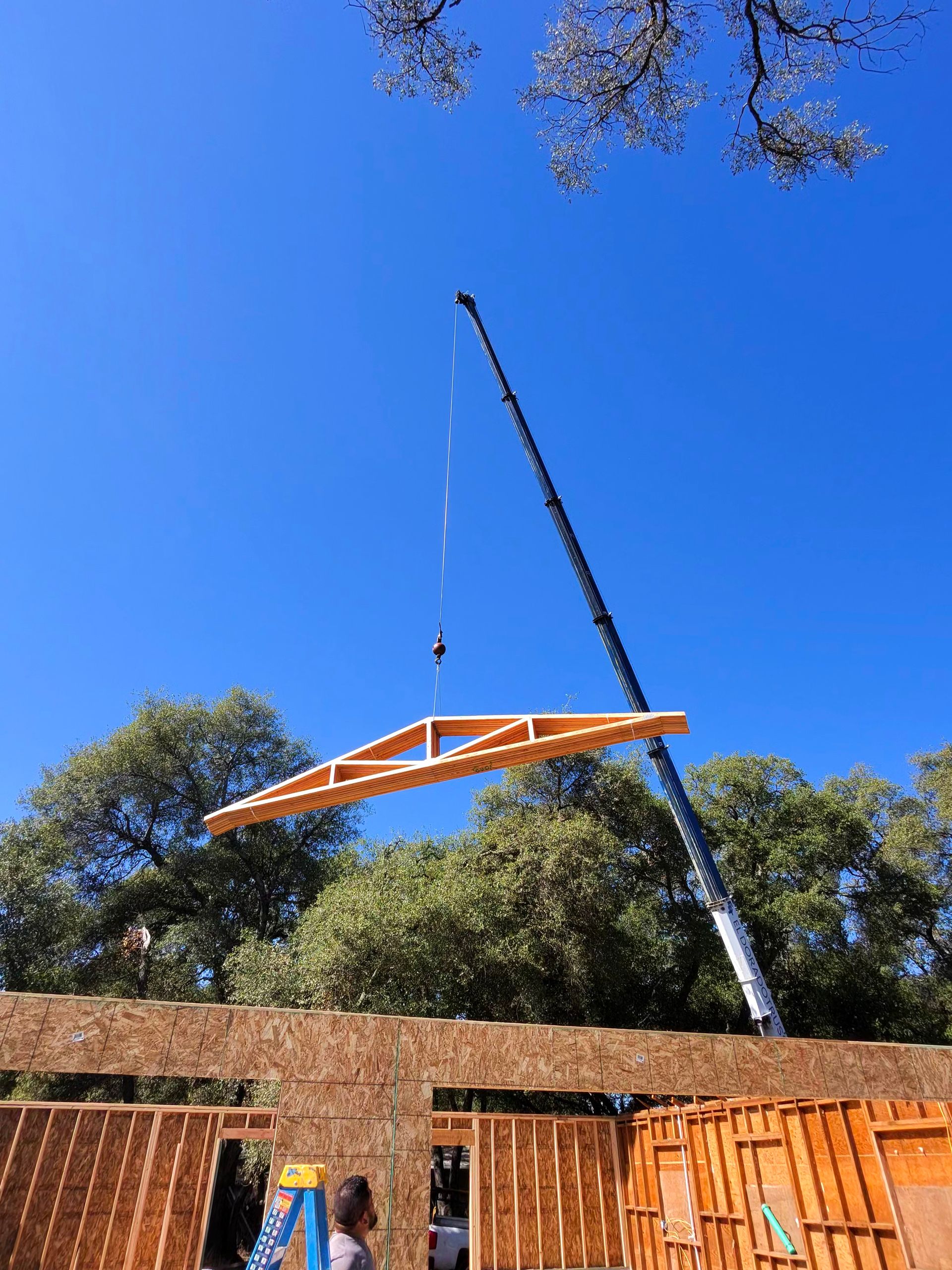 Orange canopy being lifted by a crane above a wooden structure under a blue sky