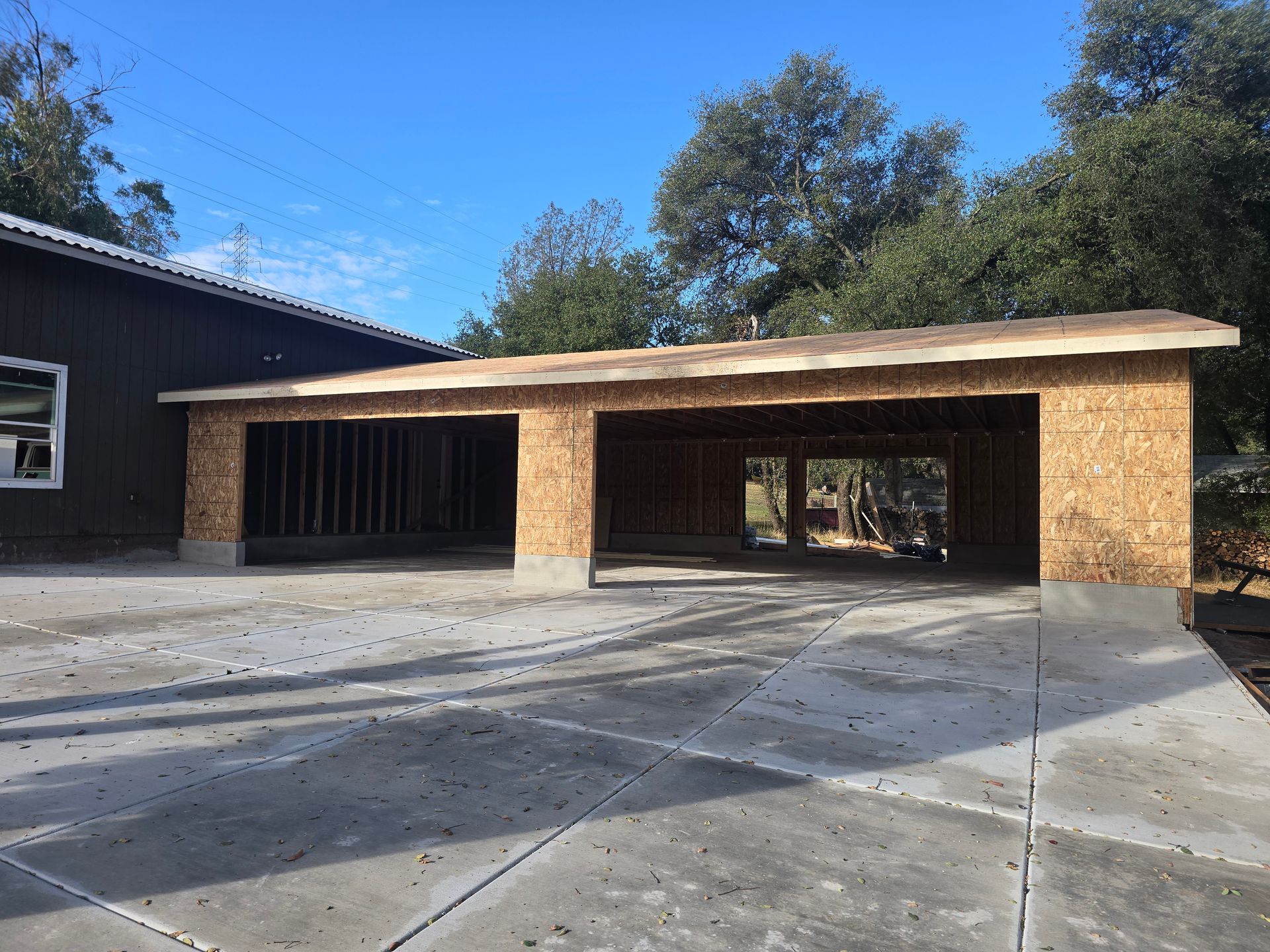 Covered driveway and carport beside a house, with concrete pavement and trees in the background