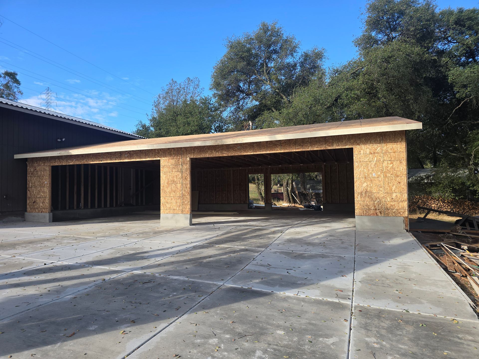 Partially built brick carport beside a house, with a concrete driveway and trees in the background