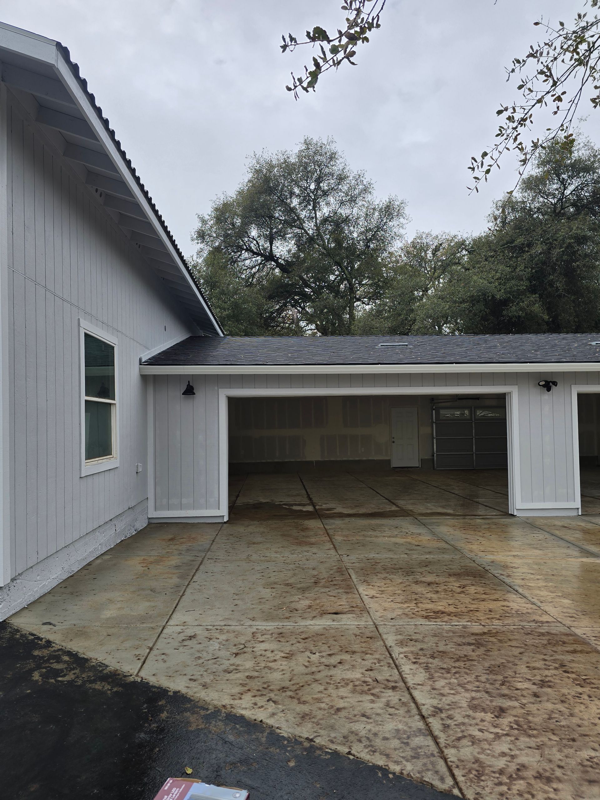 Concrete driveway and open garage attached to a gray house under an overcast sky
