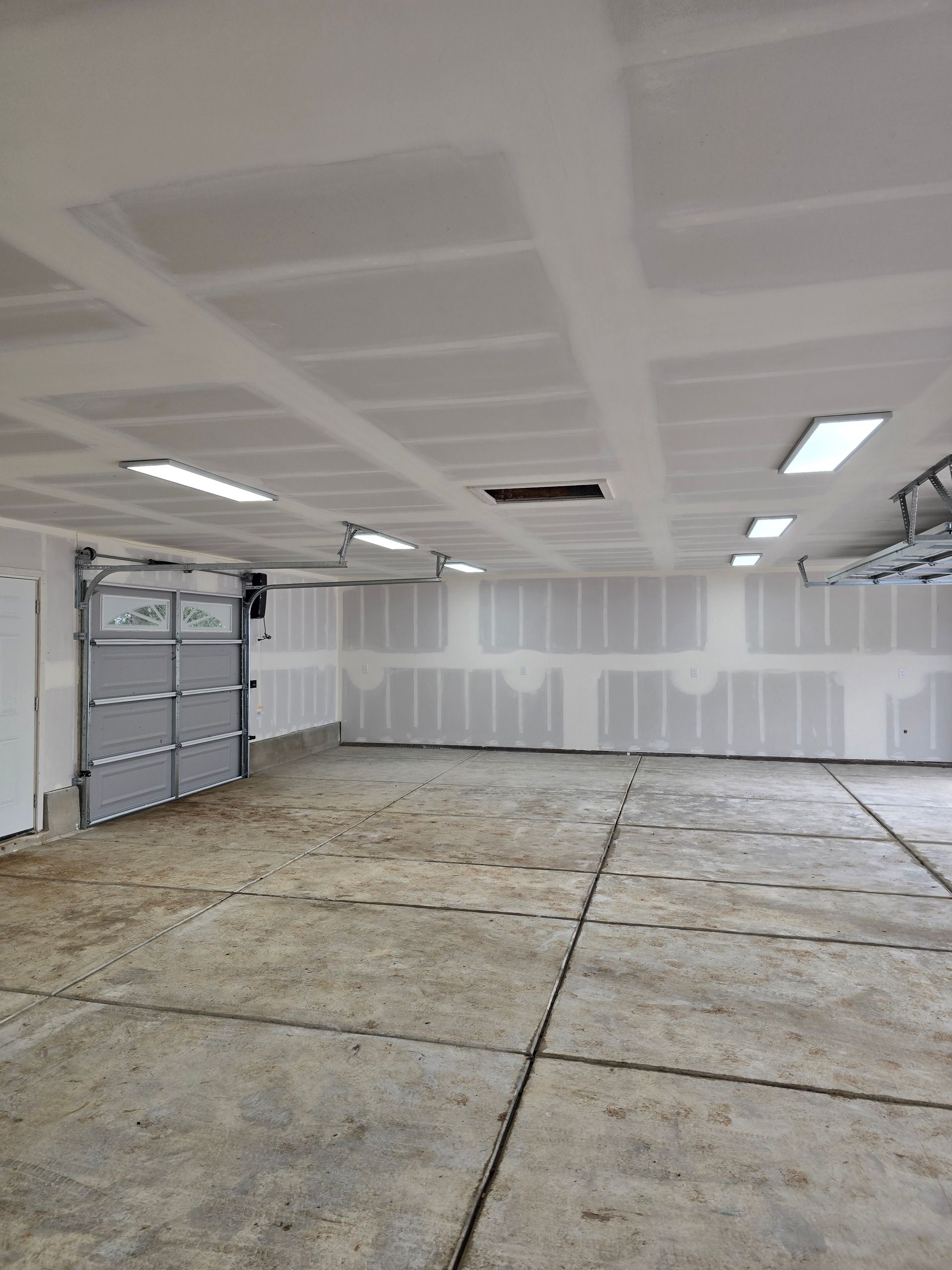 Empty garage interior with unfinished floor, white walls, ceiling lights, and a closed garage door
