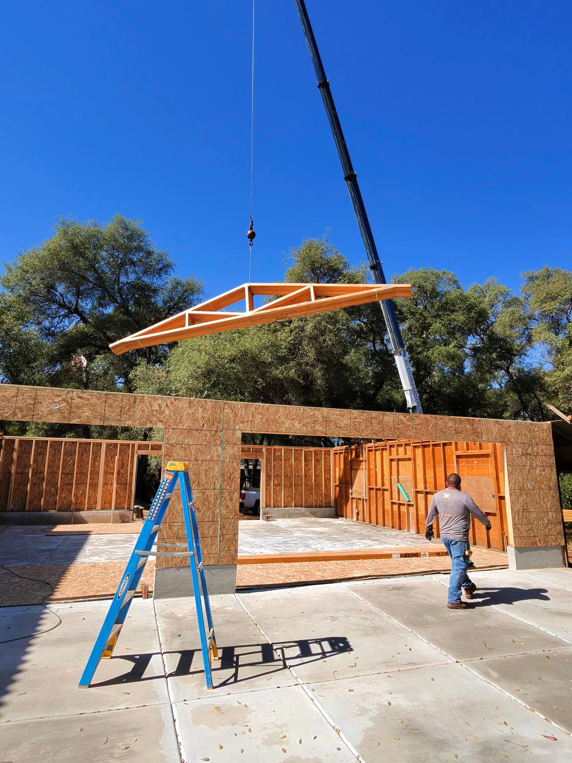 Construction site with a crane lifting a wooden roof frame above a partially built brick house