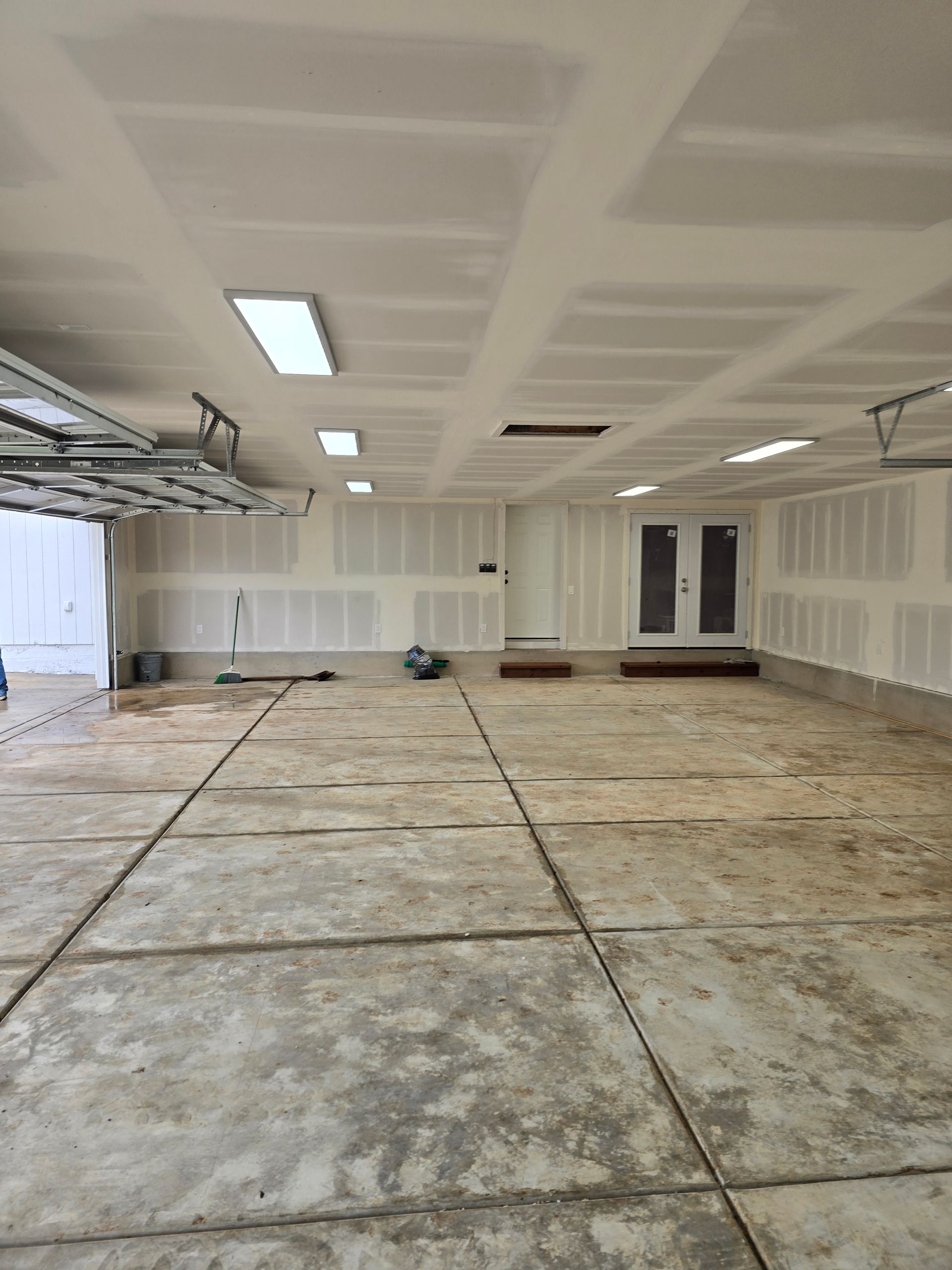 Empty unfinished garage with bare drywall, concrete floor, and overhead fluorescent lights.