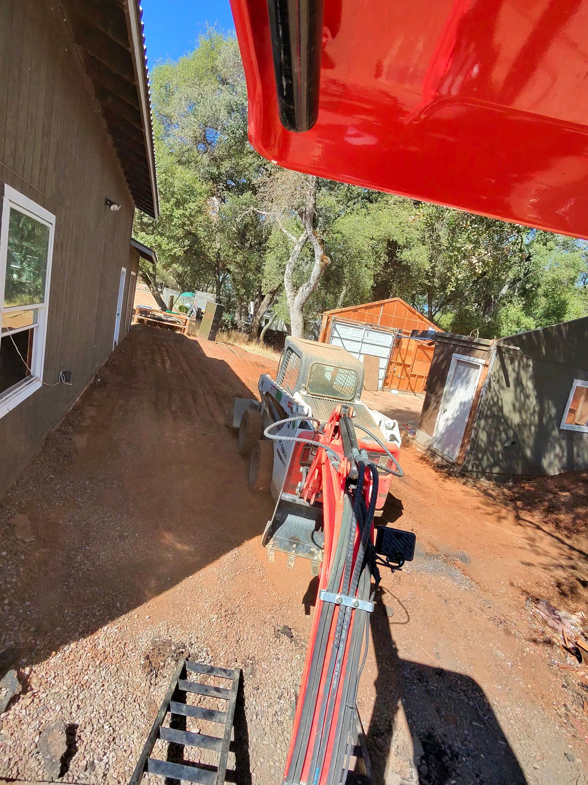 View from a red excavator digging beside a house on a dirt construction site