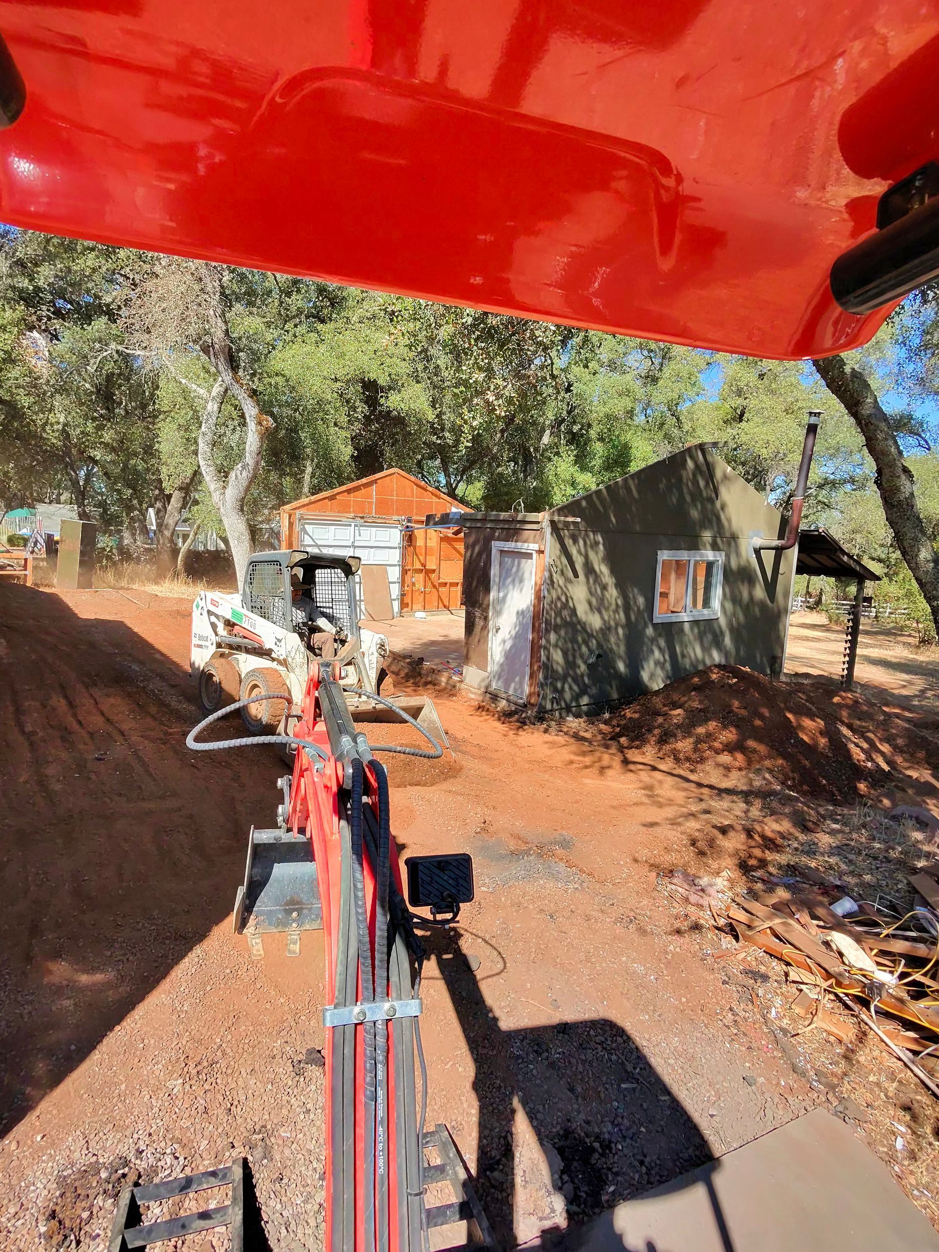 Tractor view of a dirt road leading to a small white house and orange-roofed shed in a wooded area