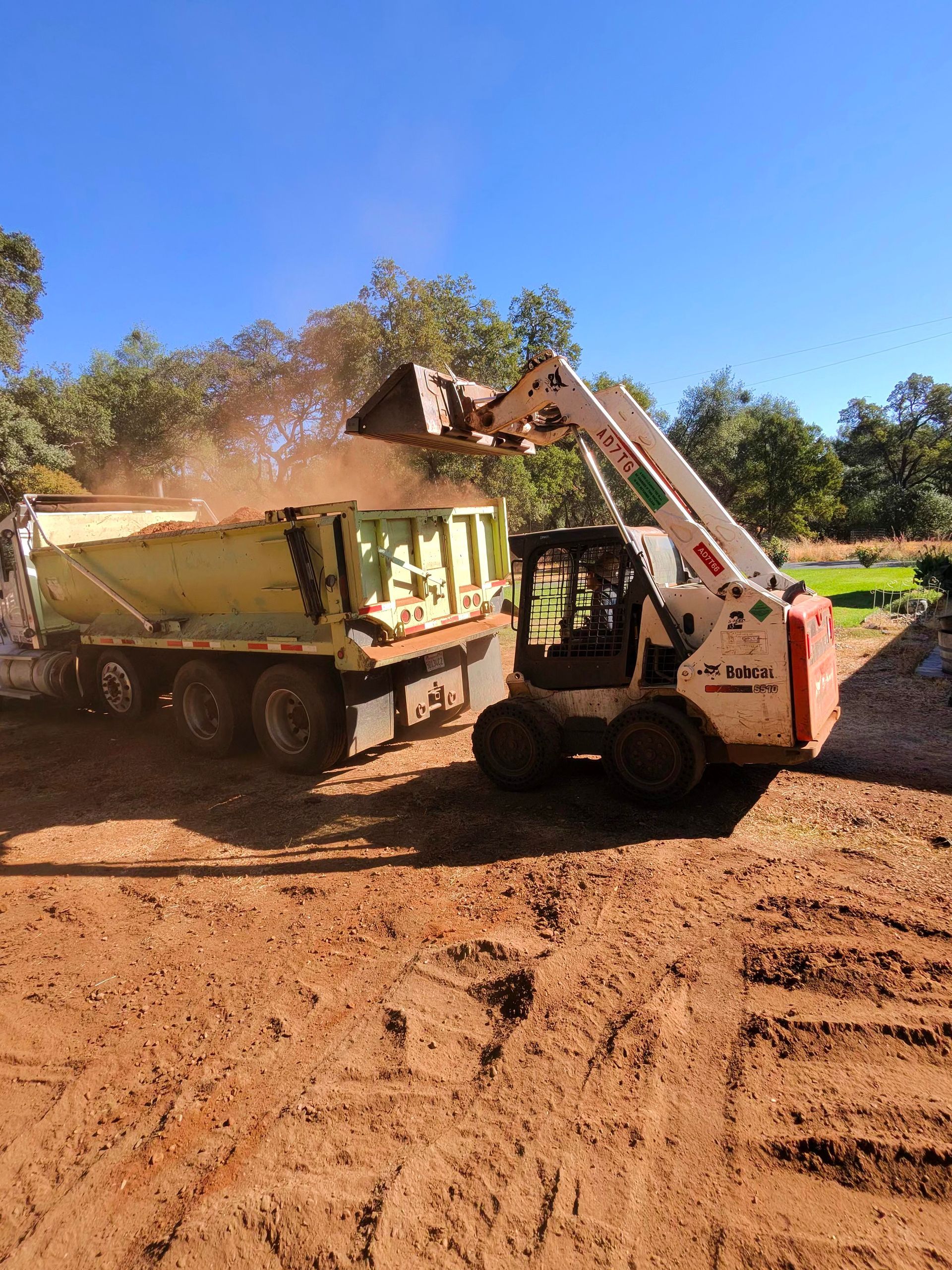 Loader dumping red dirt into a yellow dump truck on a dirt road under a blue sky