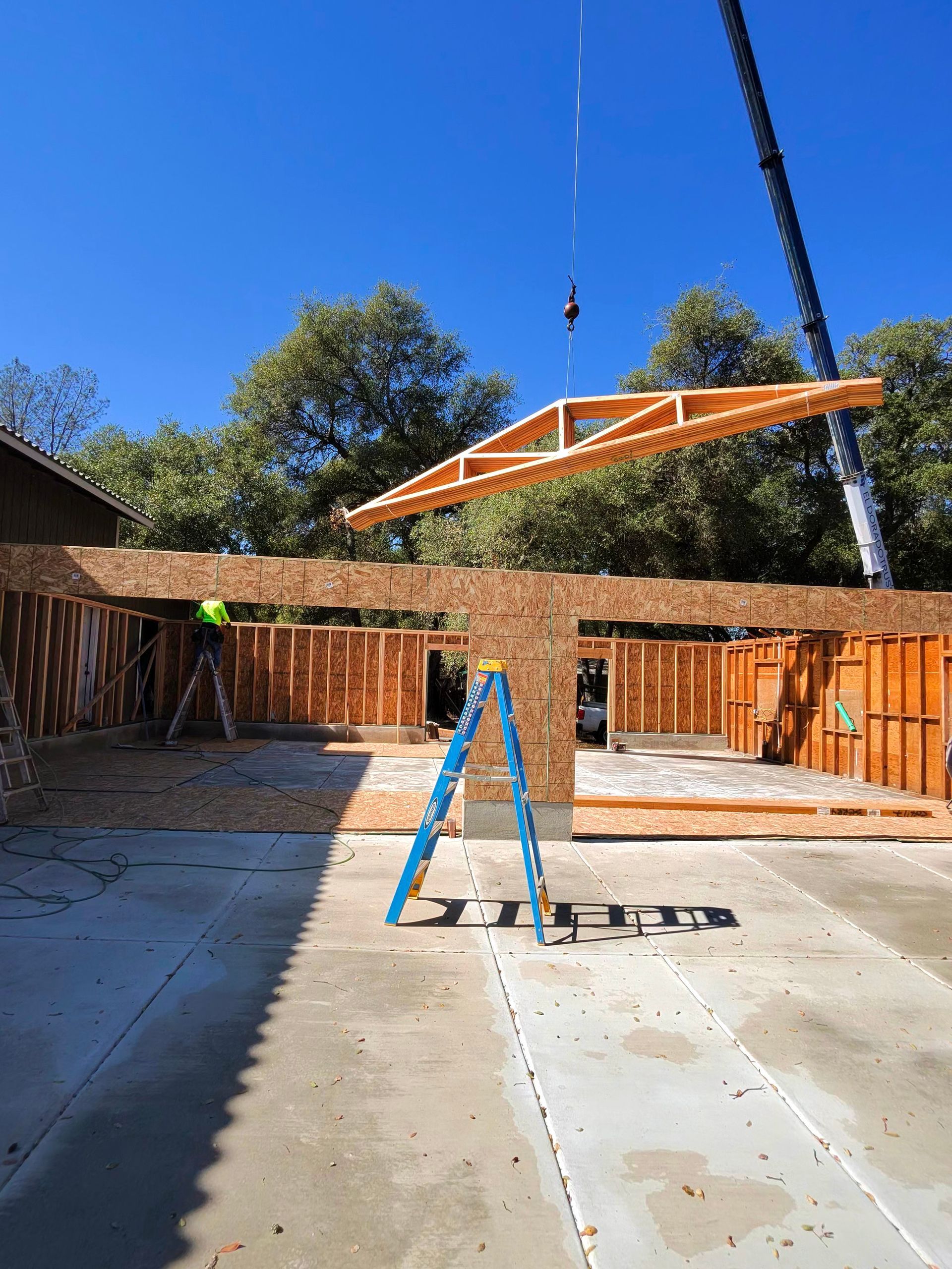 Backyard patio with a blue ladder and a crane lifting a large orange canopy frame