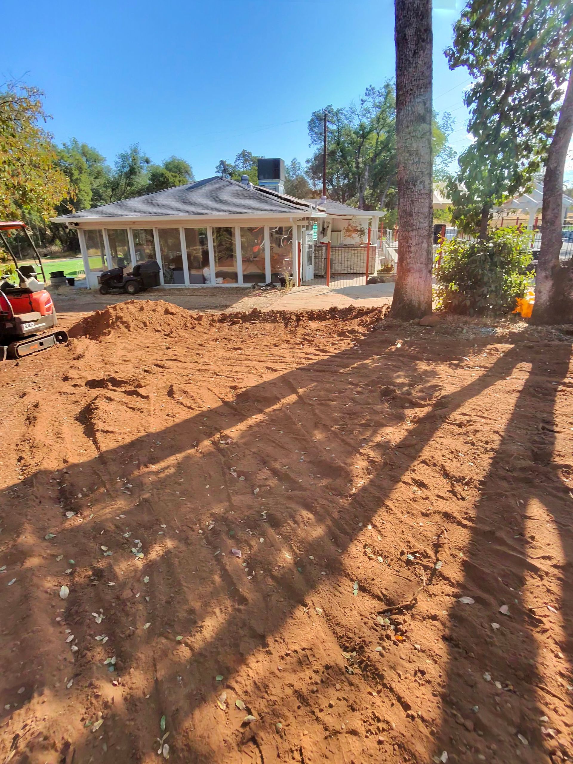 Dirt-covered yard beside a white house with columns, trees casting long shadows in bright sunlight.