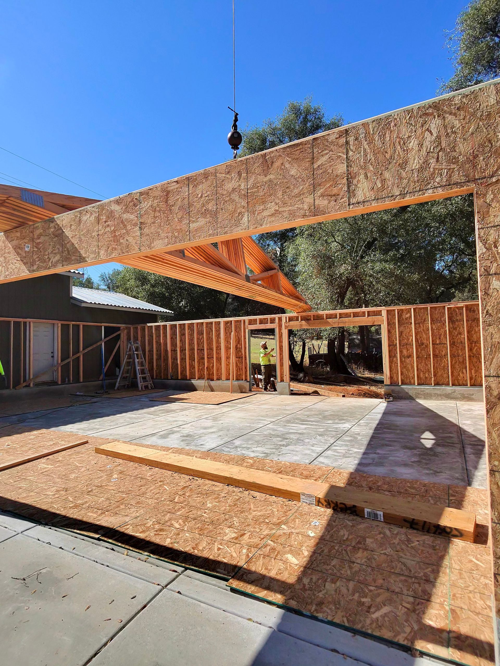 Partially constructed wooden patio with exposed beams and concrete floor under a blue sky