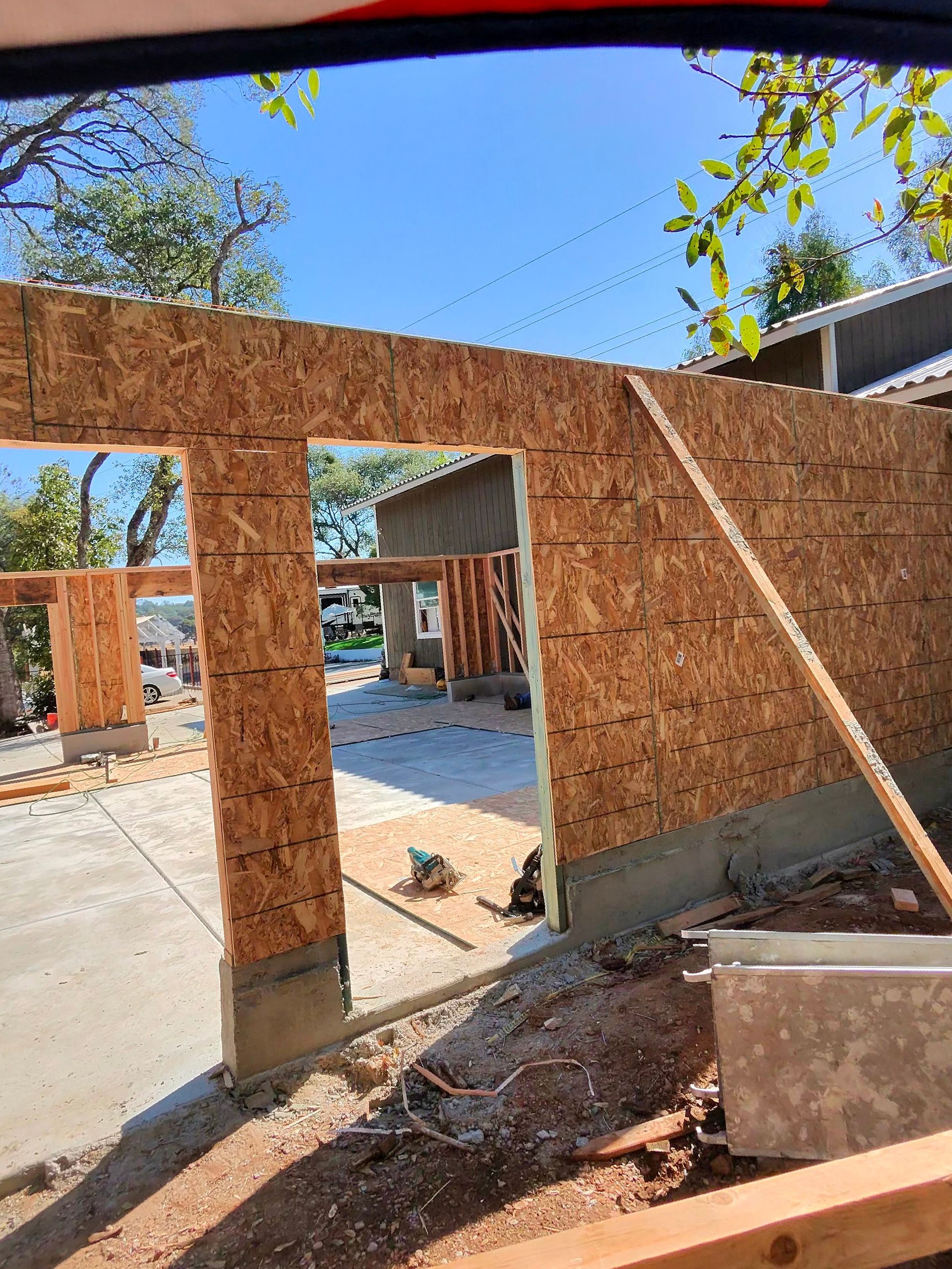 Partially framed house under construction with OSB walls, doorway, and debris on a concrete slab