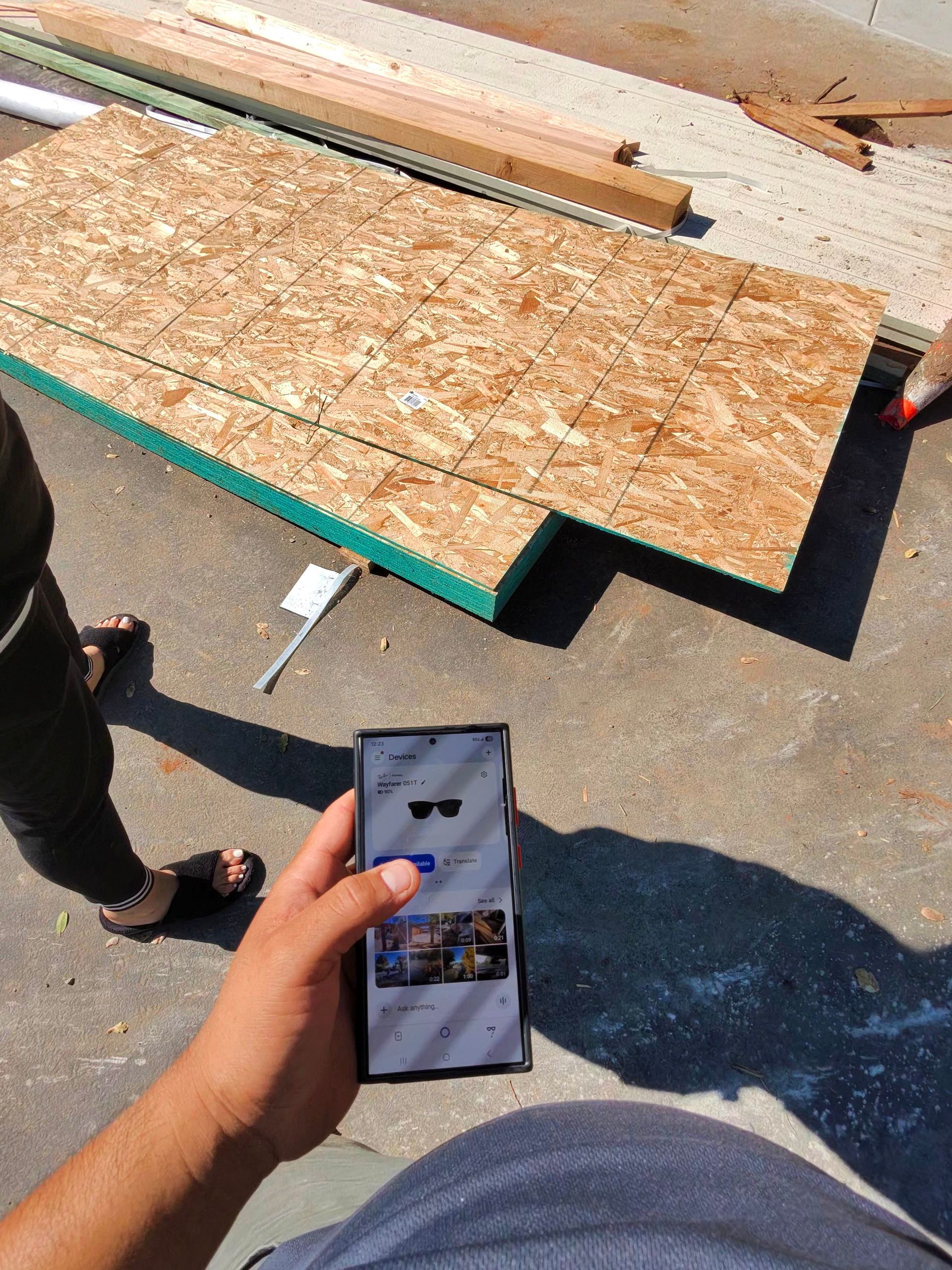 Person holding a phone at a construction site beside plywood boards on pavement