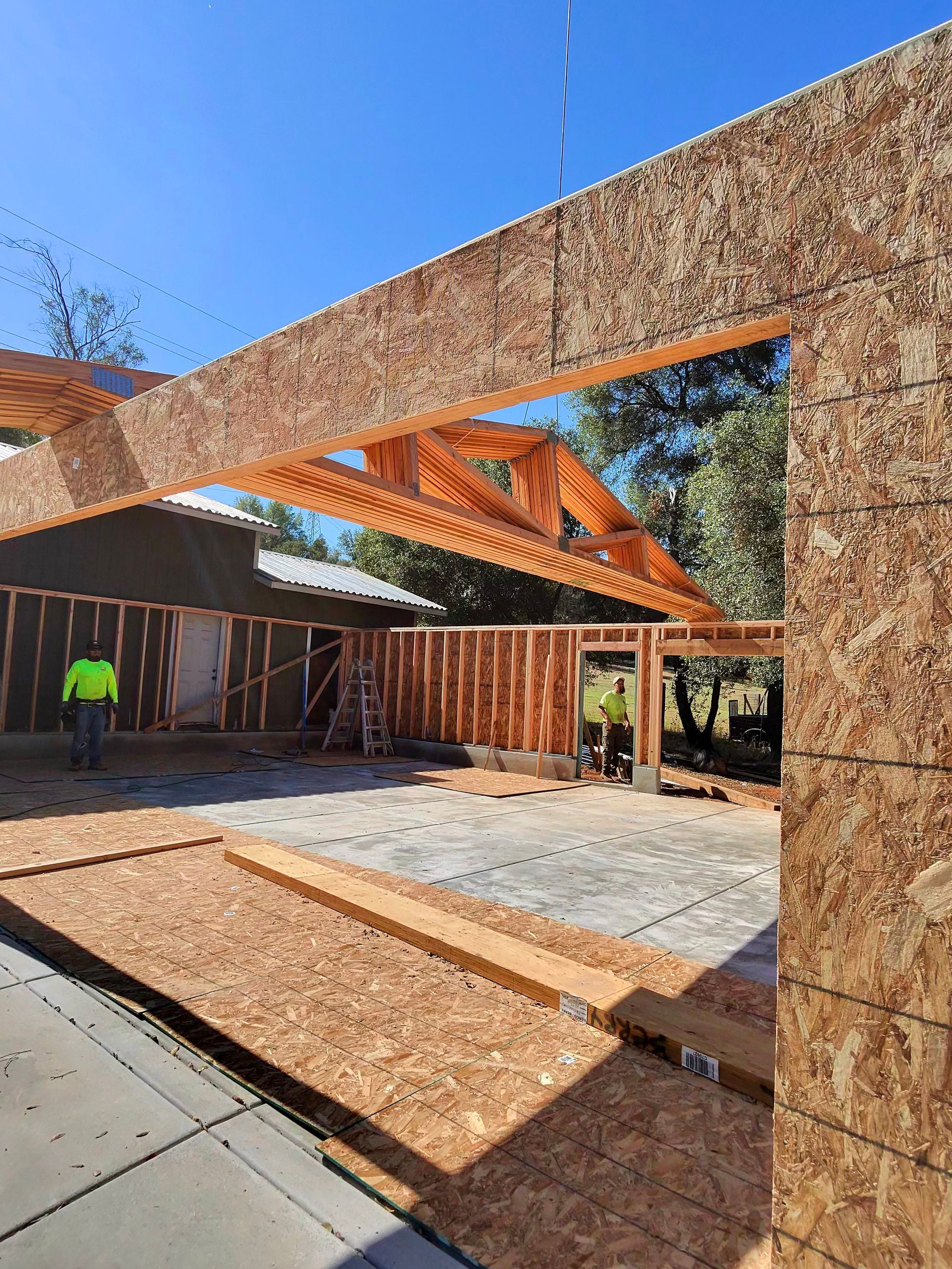 Partially built wooden structure with exposed beams and stone walls in a sunny courtyard