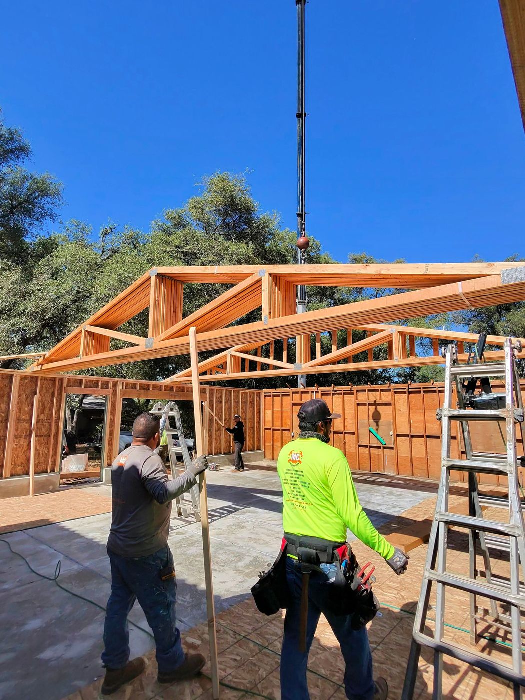 Workers assembling a wooden roof frame at a residential construction site under a clear blue sky