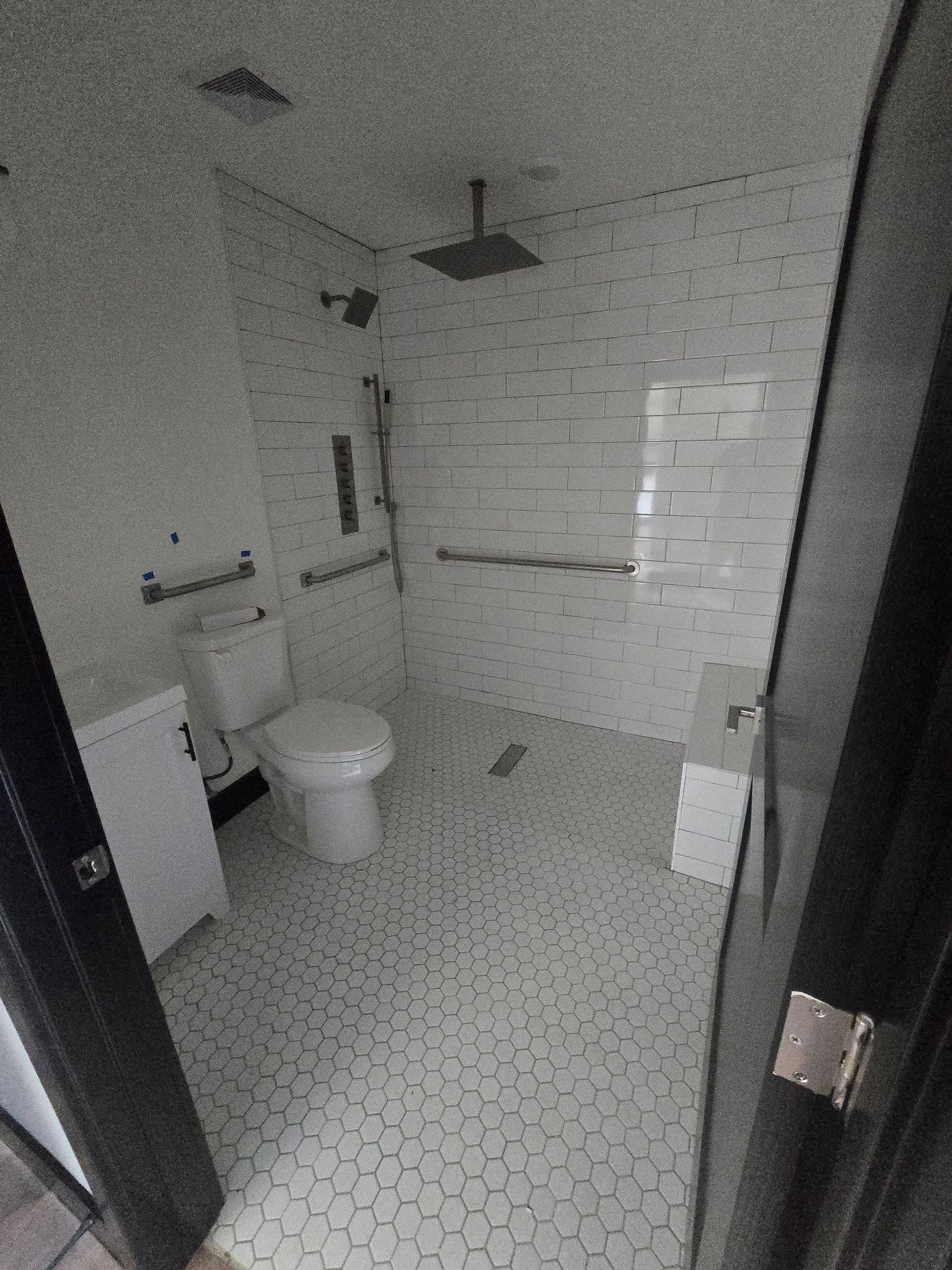 Small white bathroom with shower, toilet, tiled floor, and sink seen through an open door