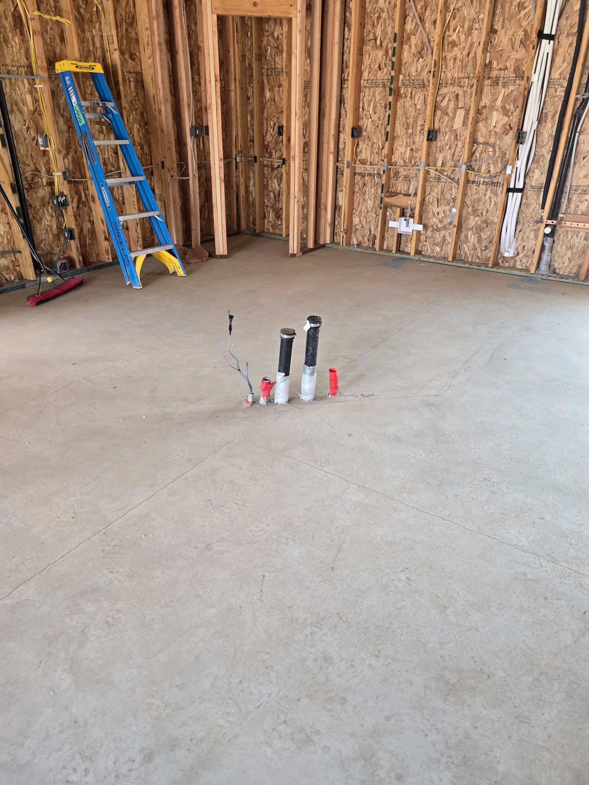 Unfinished room with exposed wood walls, a blue ladder, and small items on the concrete floor.