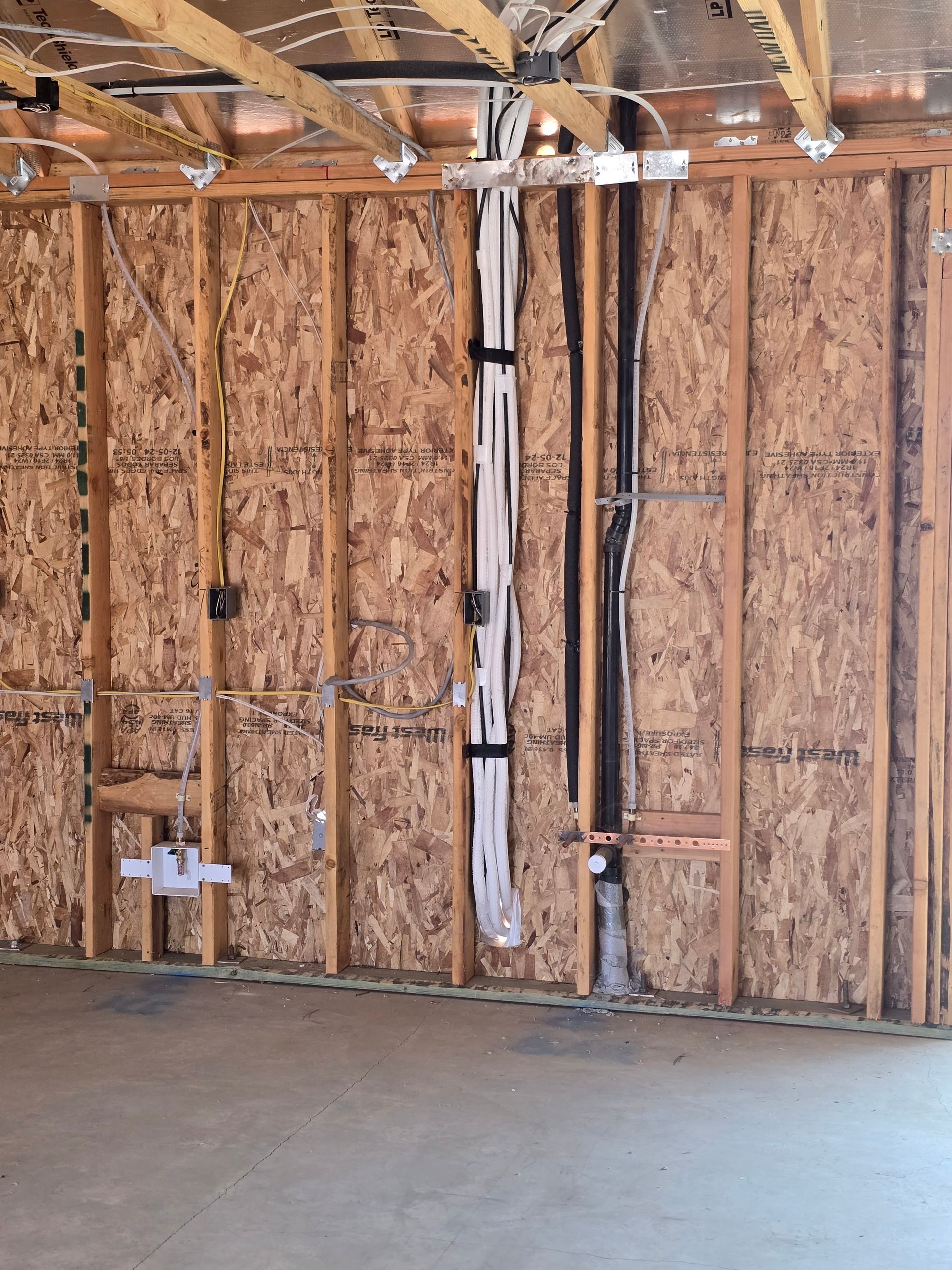 Bare garage wall with exposed studs, insulation, wiring, and concrete floor