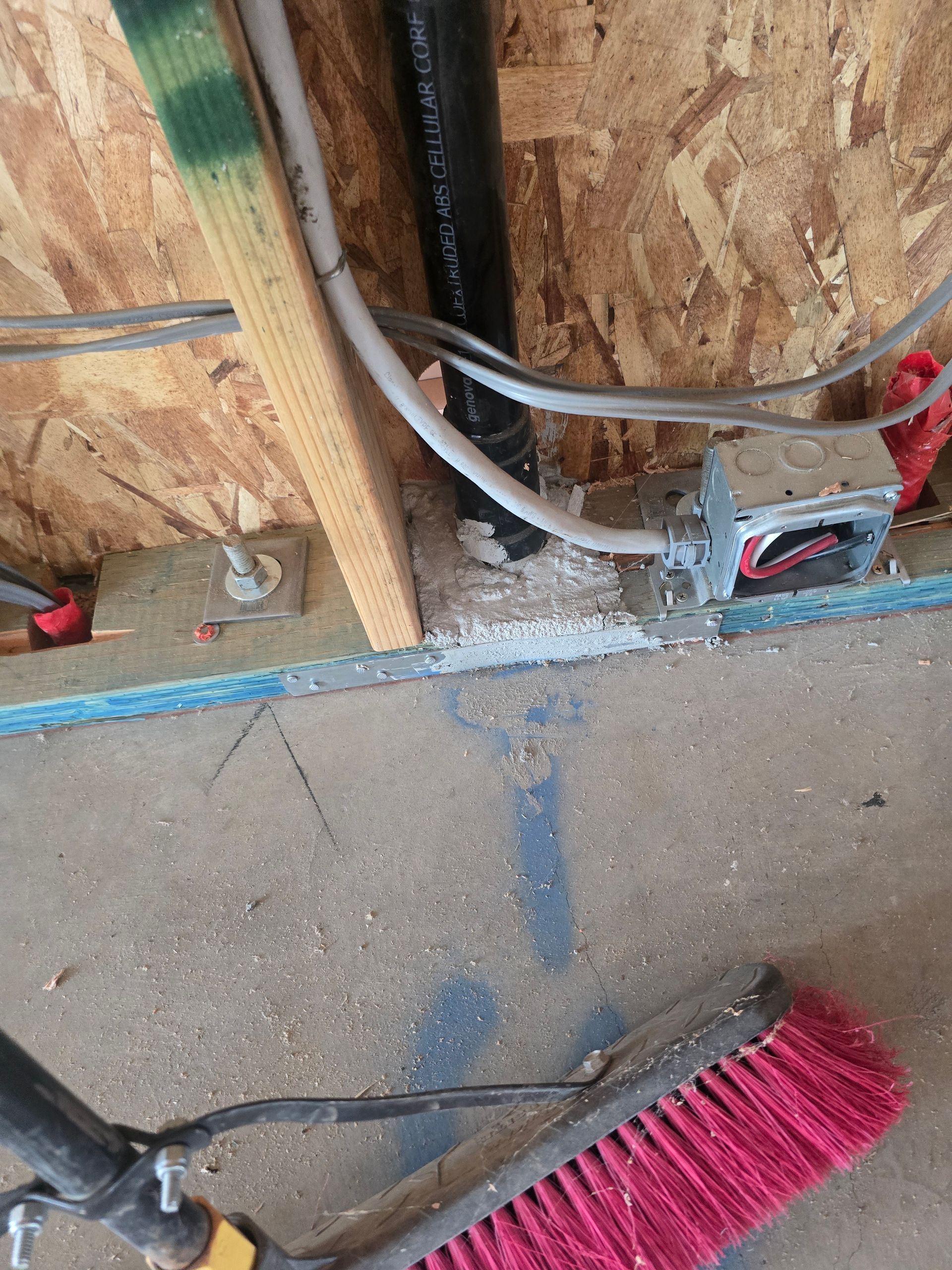 Exposed wall wiring and electrical box at floor level beside a broom in an unfinished room