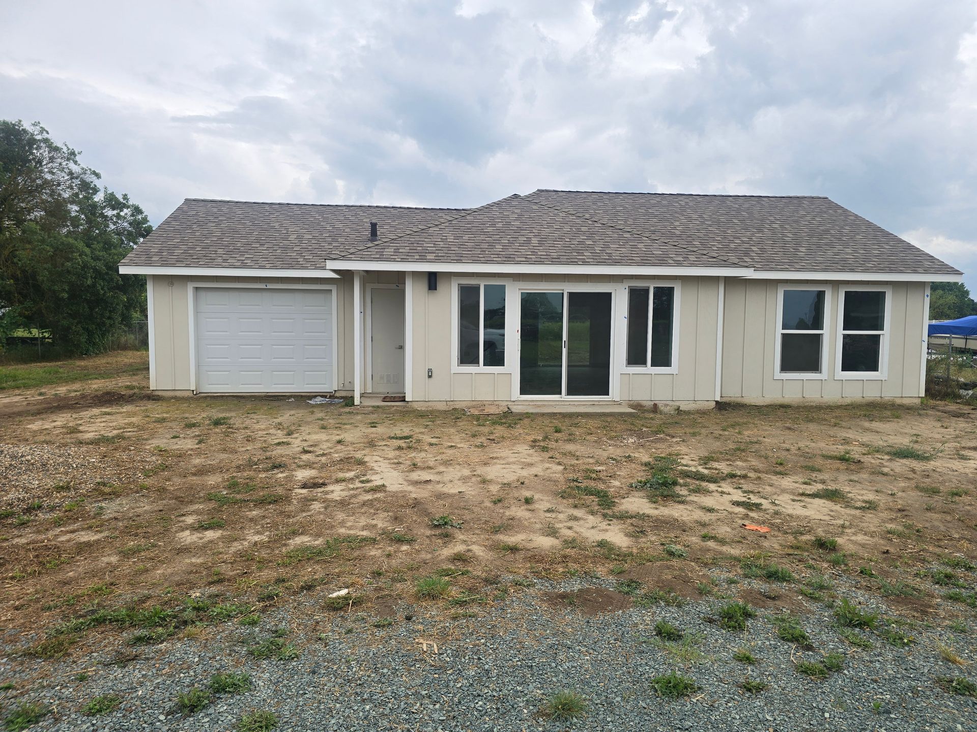 Single-story white house with gray roof, garage, and large front windows on a bare dirt lot.