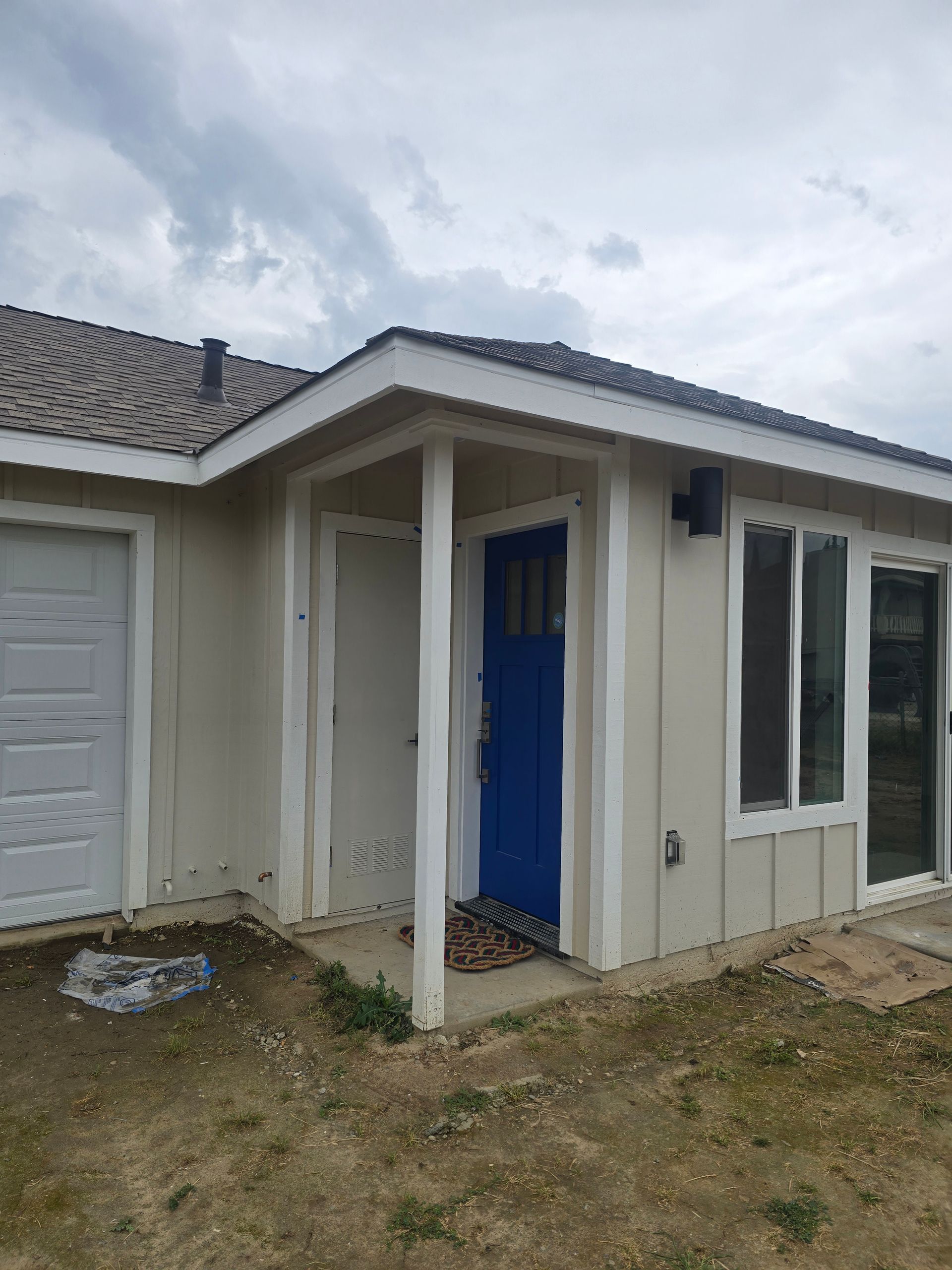 Small white house exterior with blue front door and attached garage under a cloudy sky