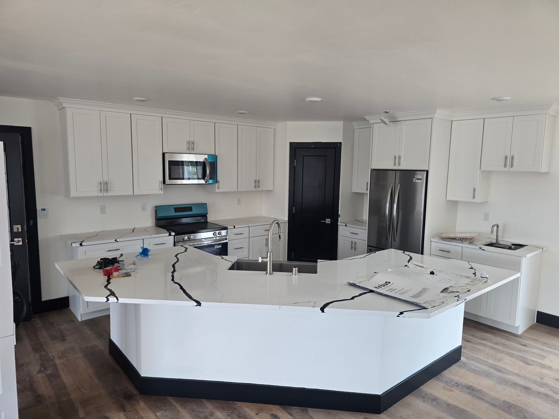 Bright white kitchen with black appliances, large island, and scattered tools on the countertop.