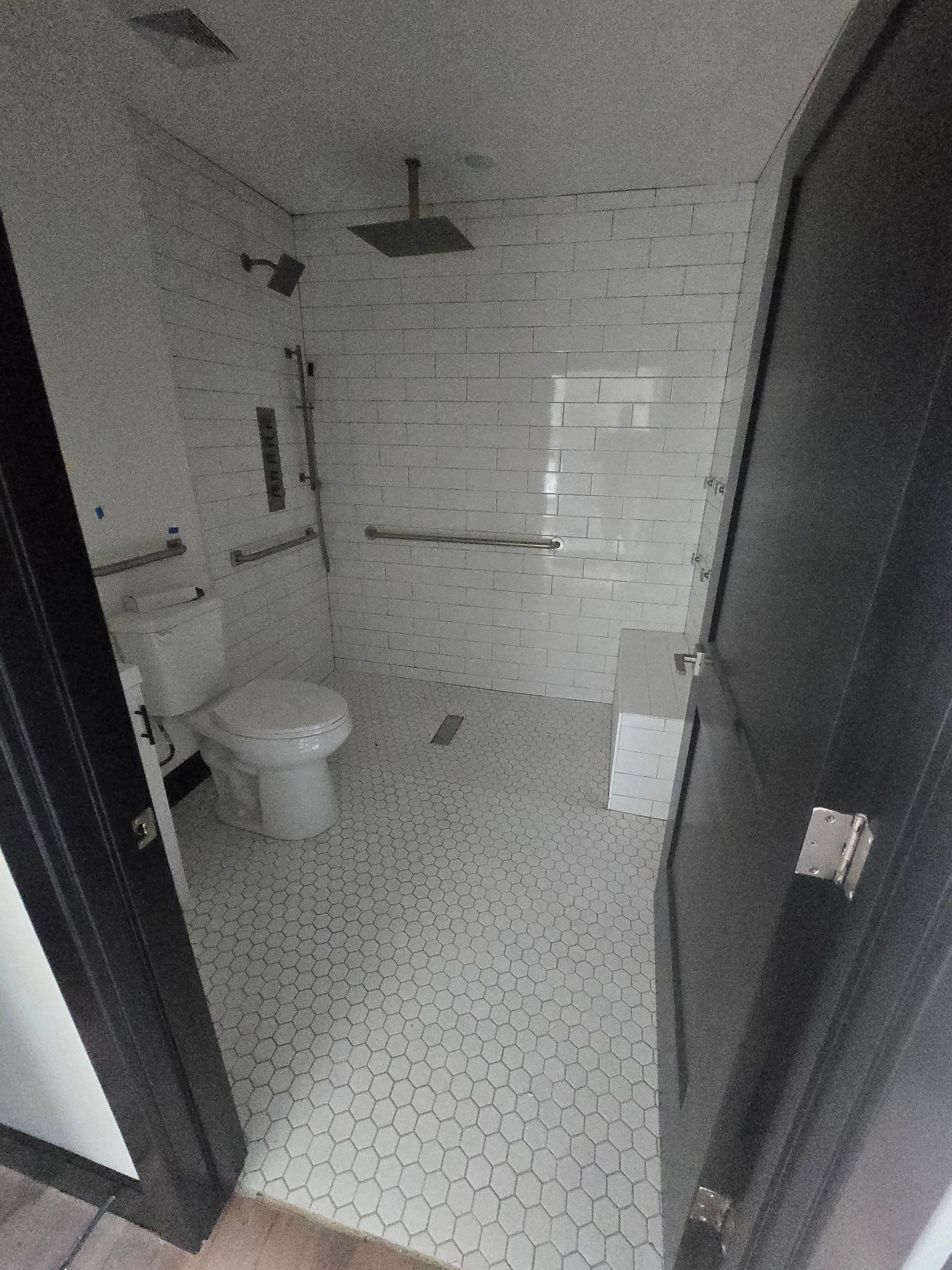Small white-tiled bathroom with a toilet, shower, and dark door frame.