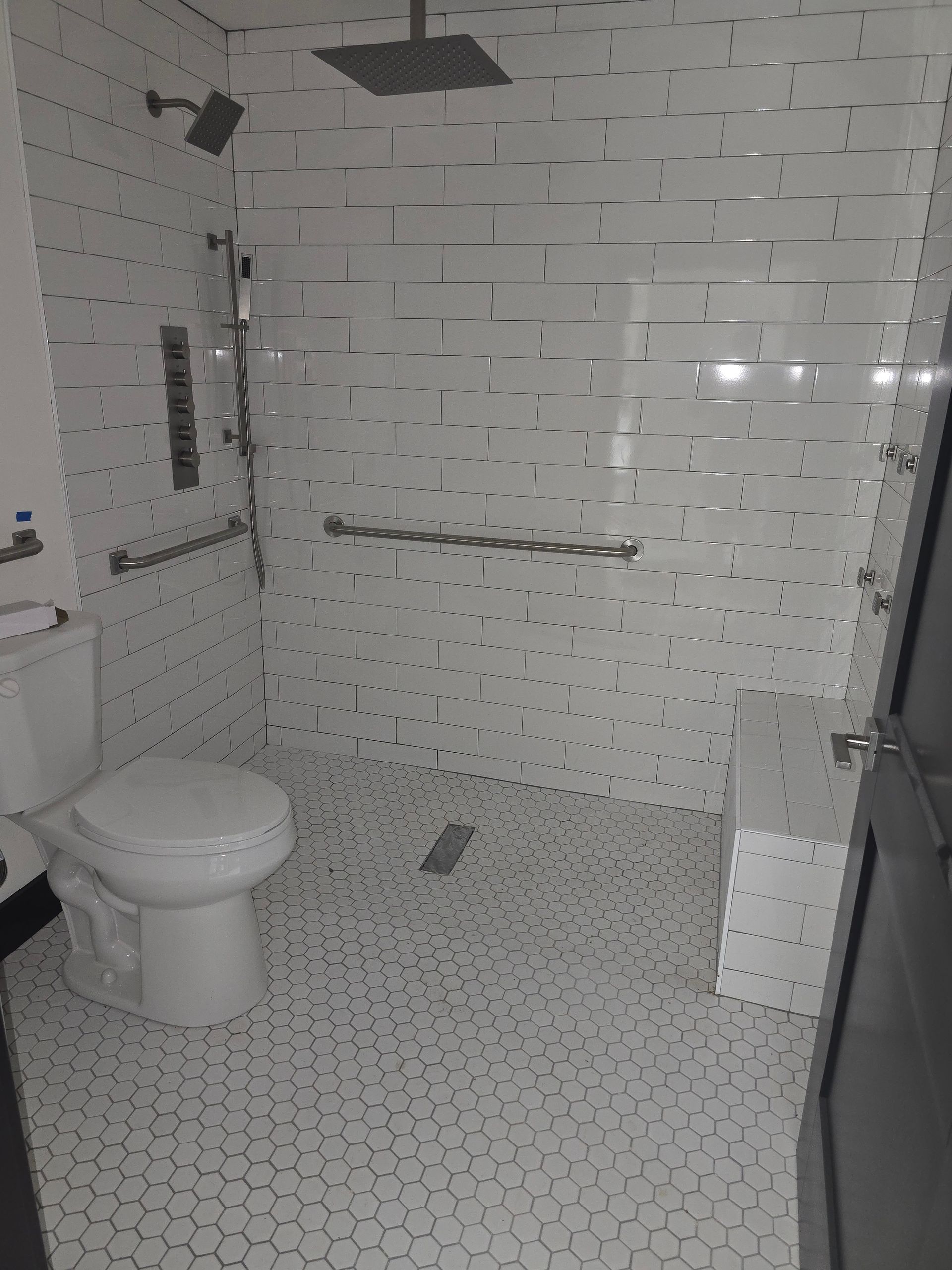 Modern white-tiled bathroom with a toilet, walk-in shower, and glass door.