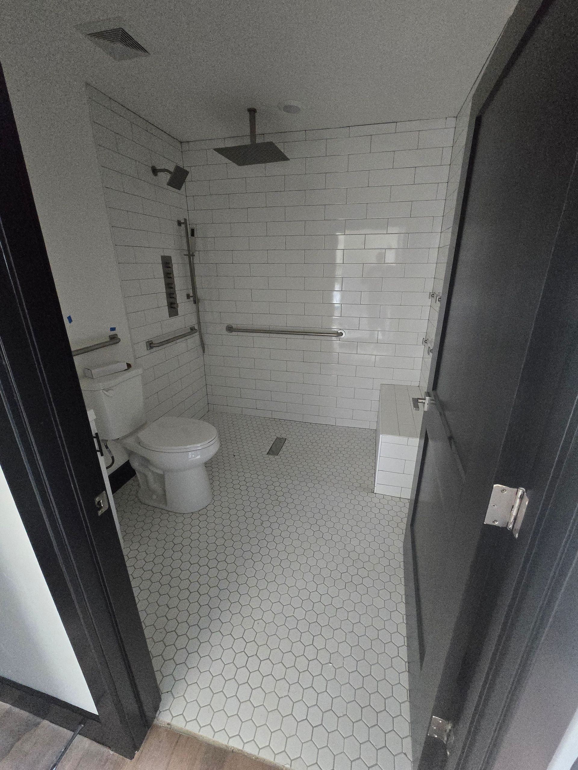 Small tiled bathroom with toilet, shower, sink, and open black door