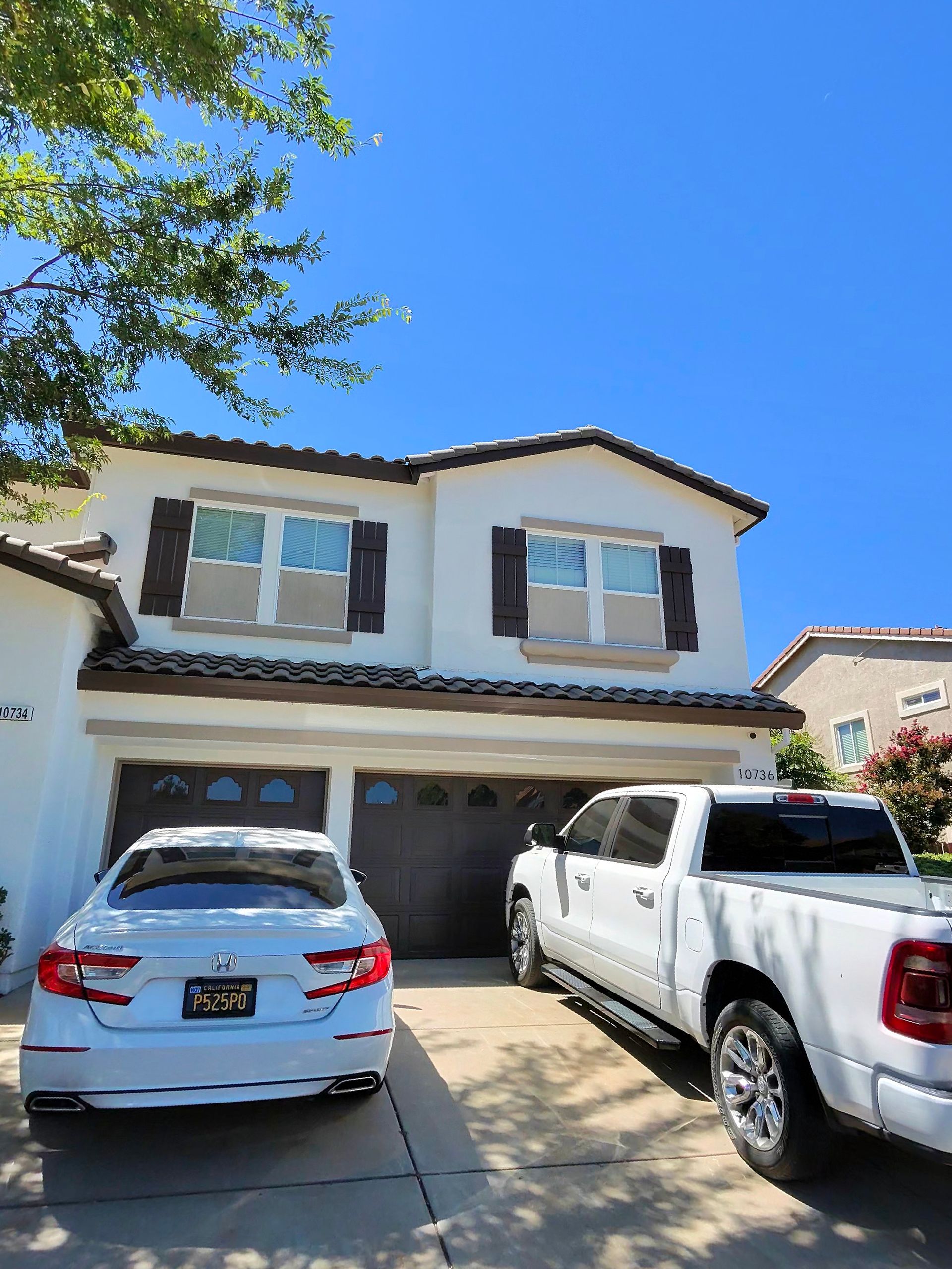 Two-story suburban house with two parked vehicles in the driveway under a bright blue sky