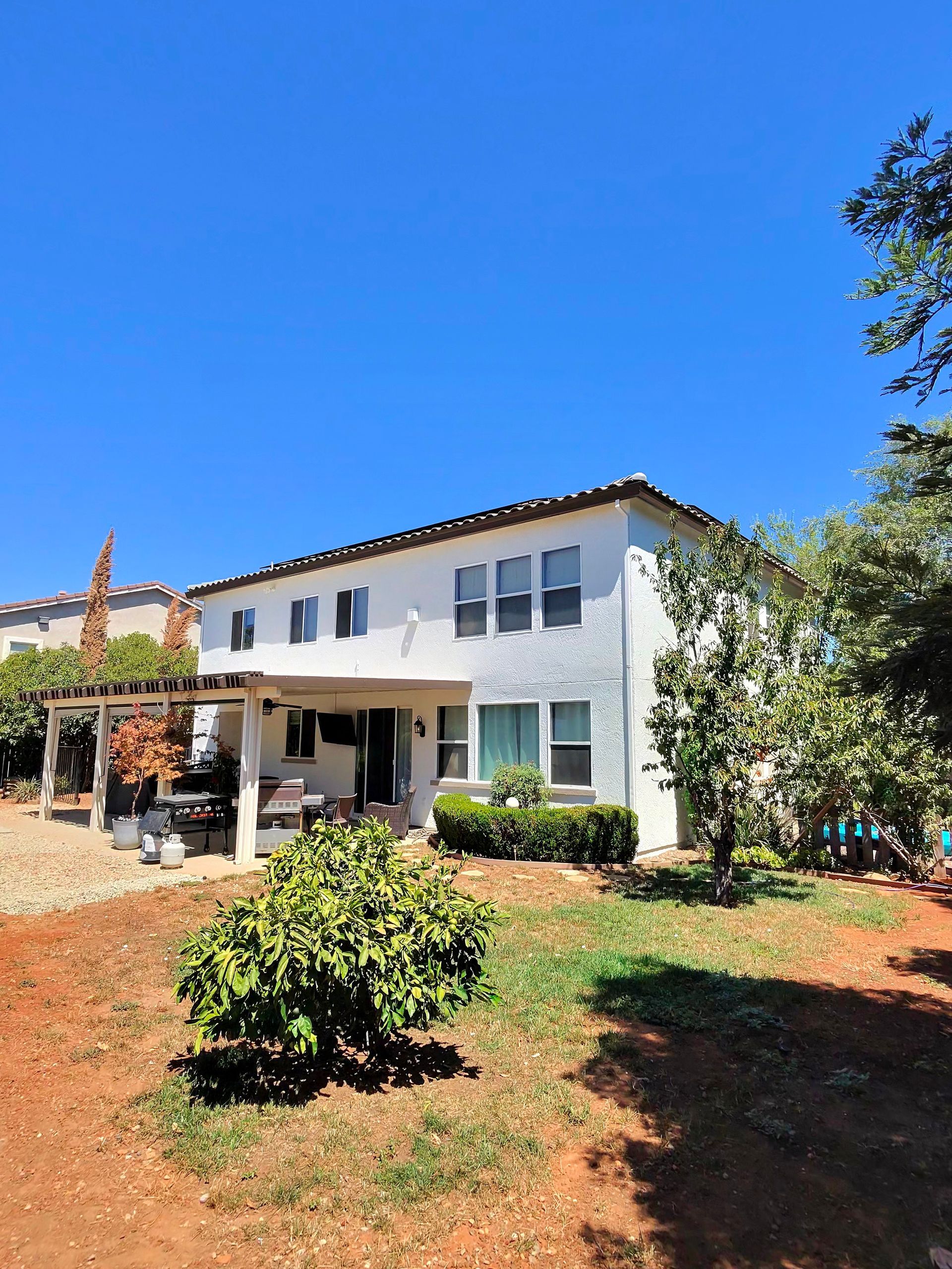Two-story white house with porch and red-brown landscaping under a clear blue sky