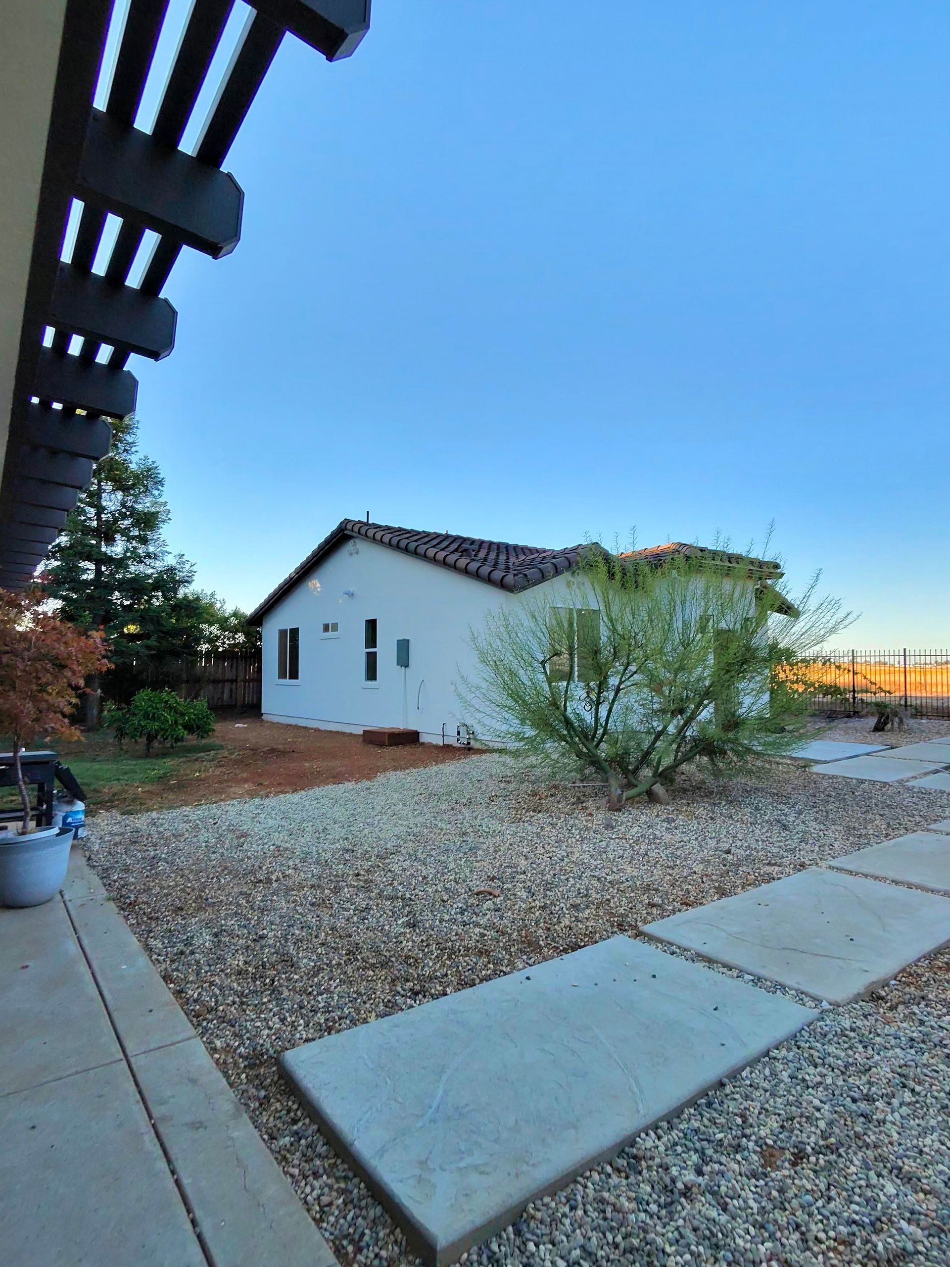 Small white house with a tiled roof, gravel yard, desert plants, and a blue evening sky.