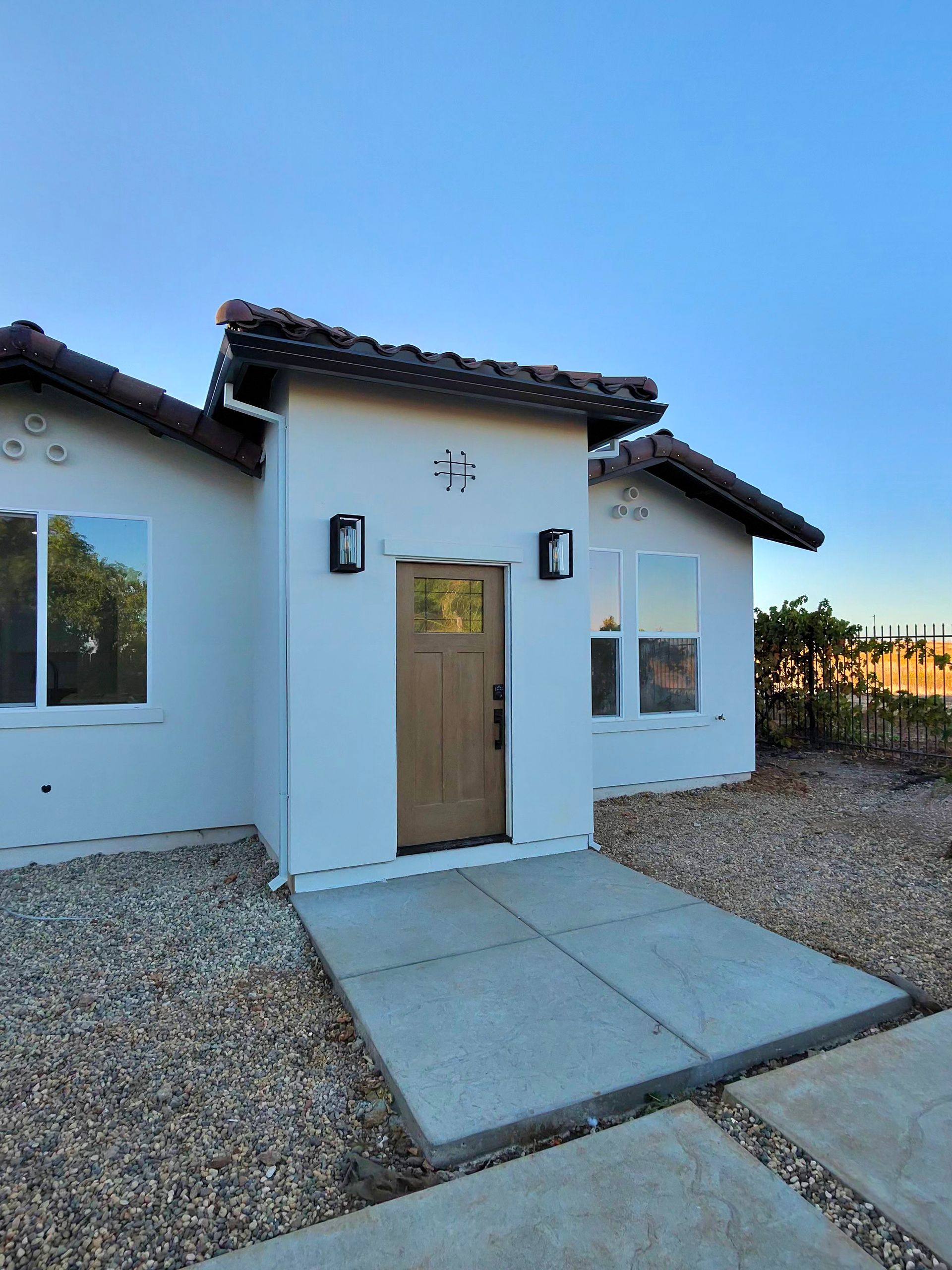 Small white house entry with a wooden door, front lights, and a concrete walkway at dusk.